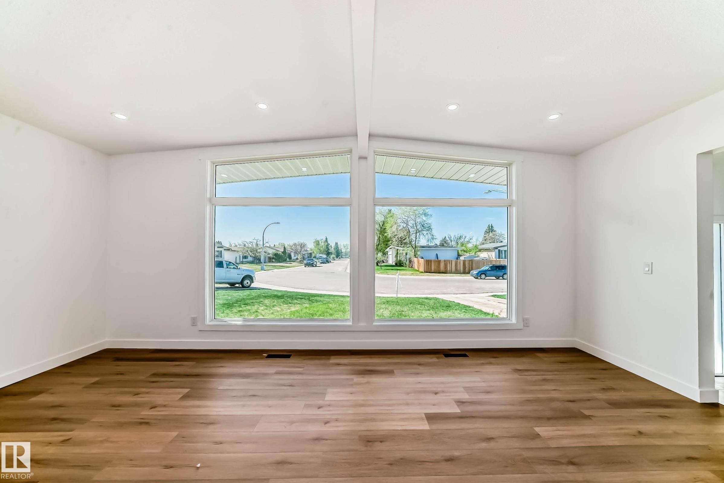 Expansive windows illuminate the interior, highlighting the rich hardwood flooring and the vaulted ceiling with recessed lighting - 7220 152A Ave, Edmonton, AB - Indoor Photo Showing Other Room