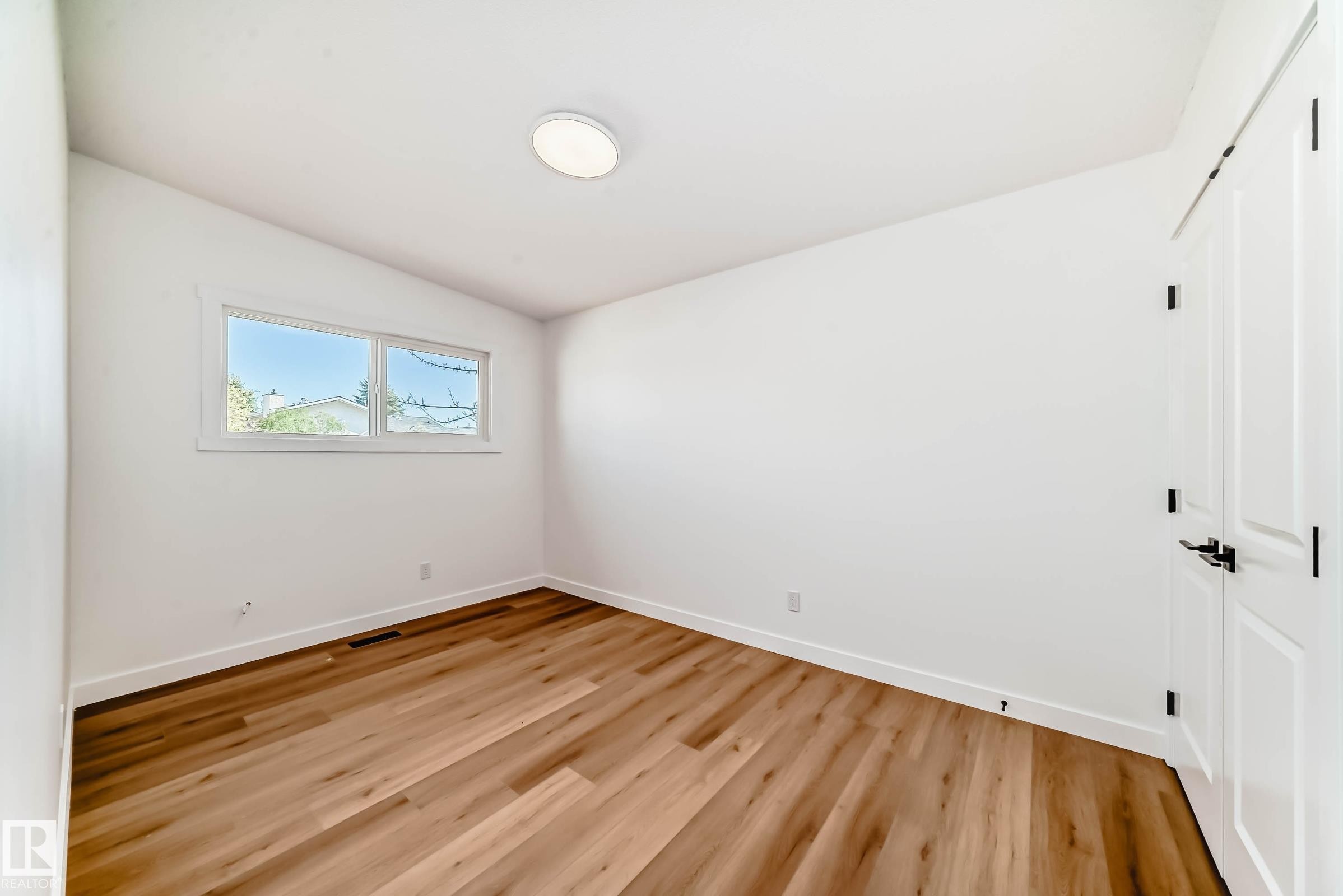 Room featuring hardwood style flooring, a window with exterior views, white walls, and a ceiling light fixture - 7220 152A Ave, Edmonton, AB - Indoor Photo Showing Other Room