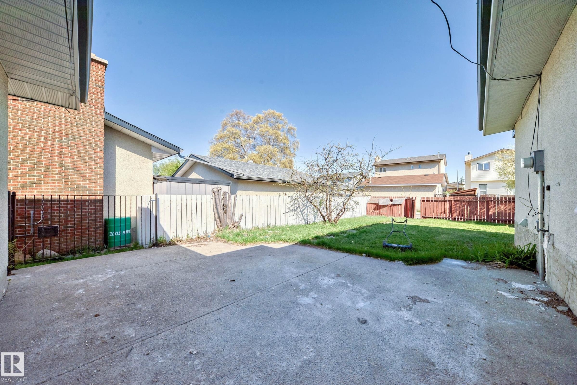 The property features a concrete patio area and an expansive lawn, partially enclosed by fencing - 7220 152A Ave, Edmonton, AB - Outdoor