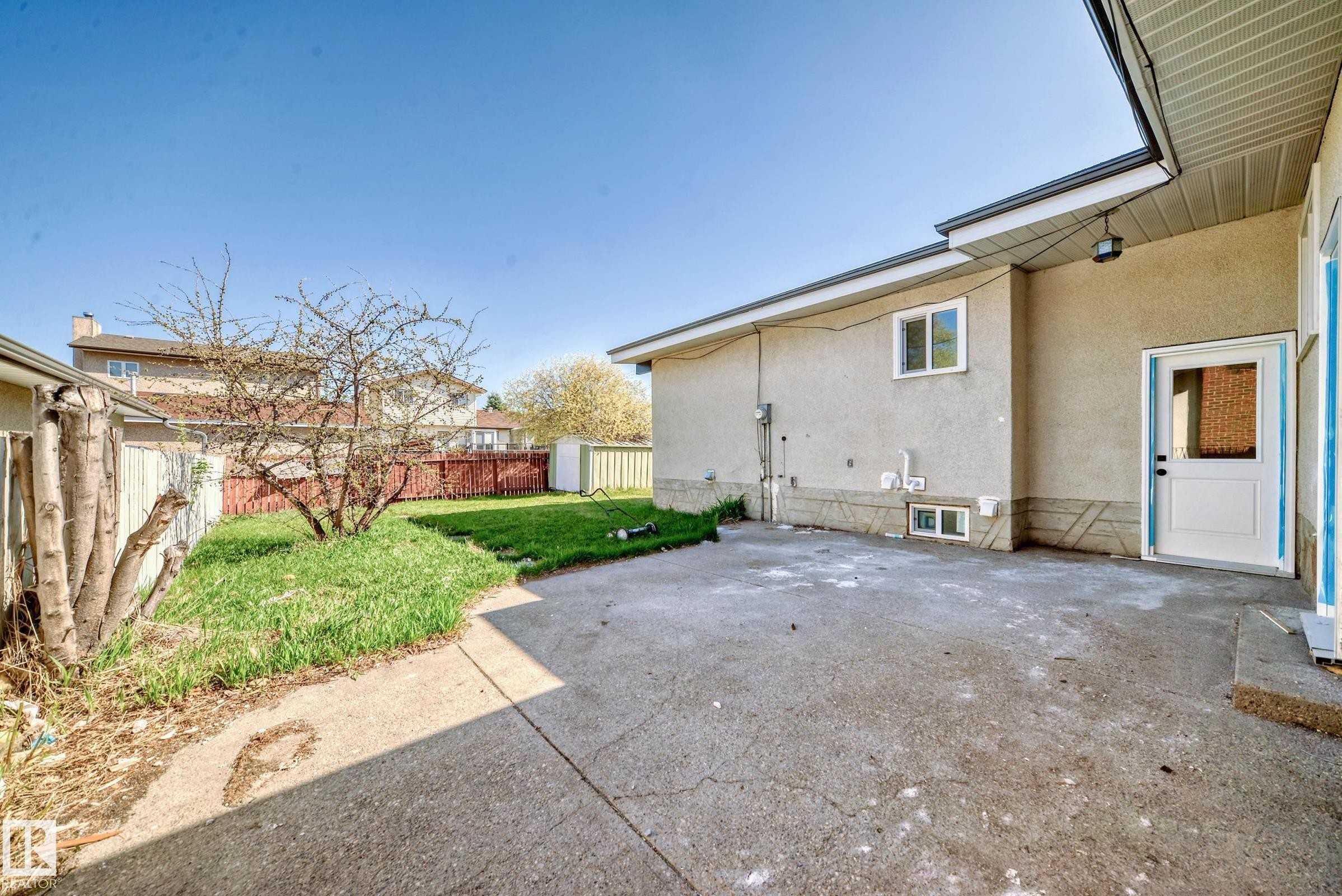 The property features a concrete patio area, a grass lawn, and a mature tree - 7220 152A Ave, Edmonton, AB - Outdoor With Exterior