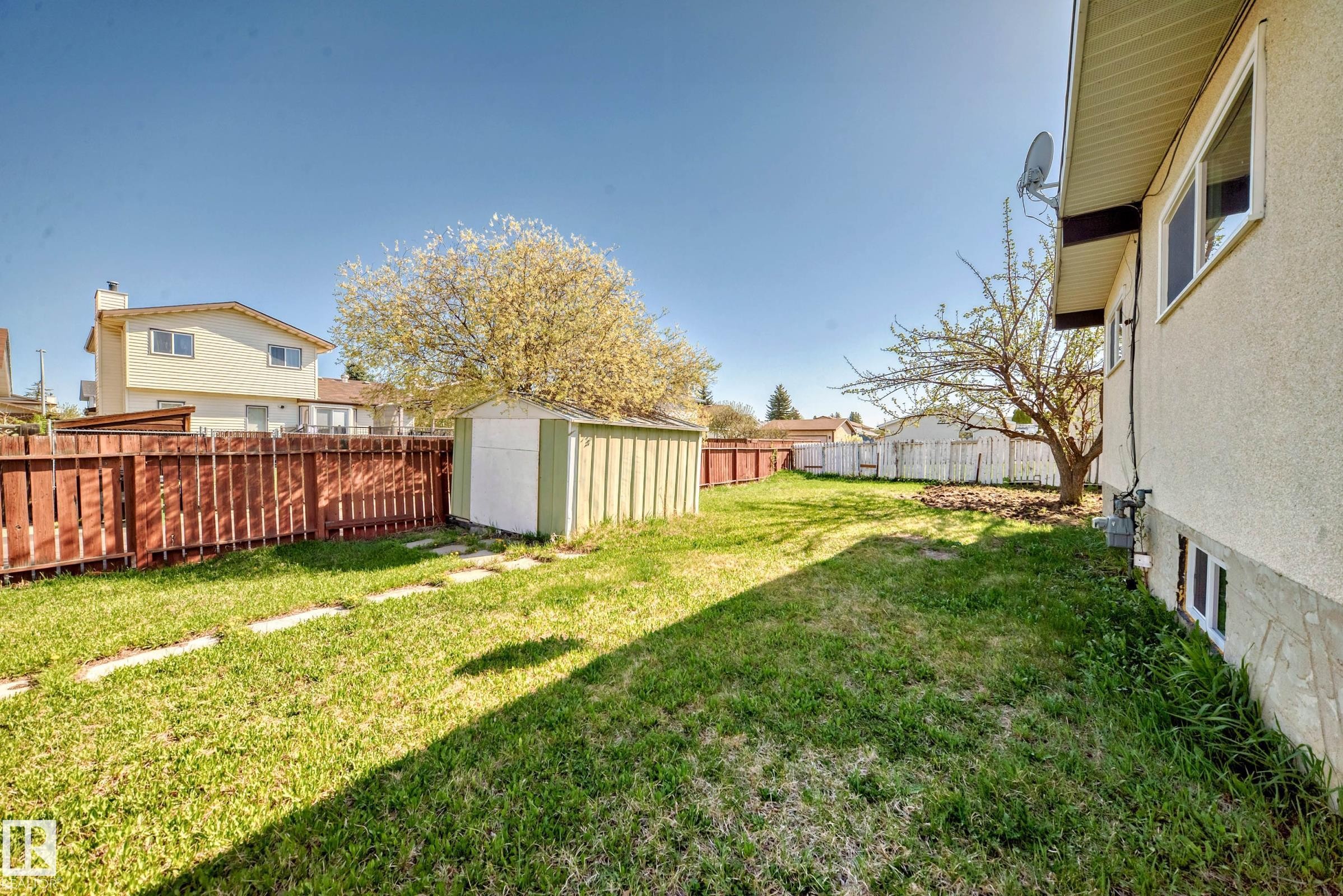 The property includes an expansive yard with a well-maintained lawn, a storage shed, and a privacy fence - 7220 152A Ave, Edmonton, AB - Outdoor
