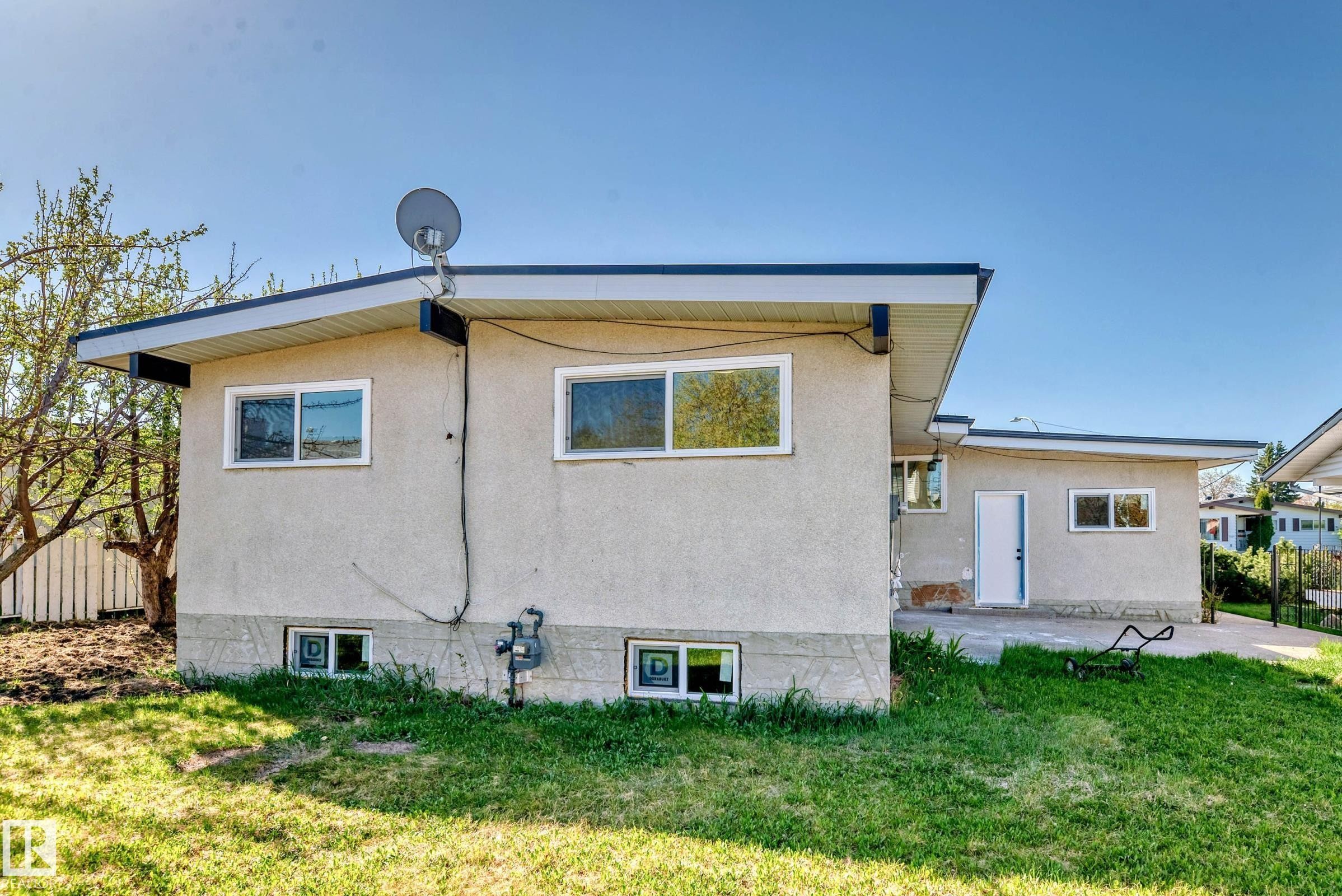 The property features a stucco exterior with multiple windows and a grass yard - 7220 152A Ave, Edmonton, AB - Outdoor