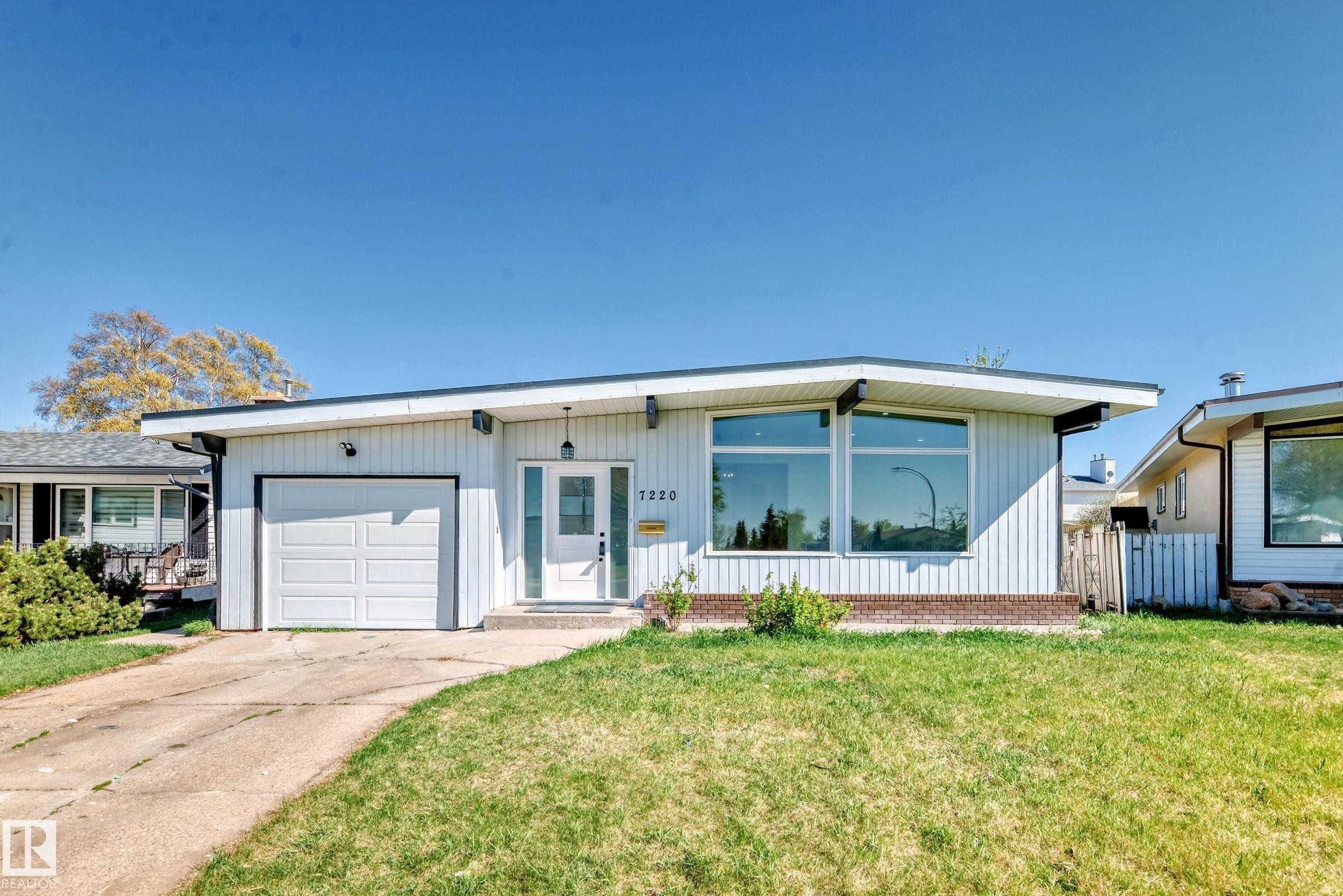 The property features a single-story design with white siding, a white garage door, and a front entrance with a white door and sidelight windows - 7220 152A Ave, Edmonton, AB - Outdoor