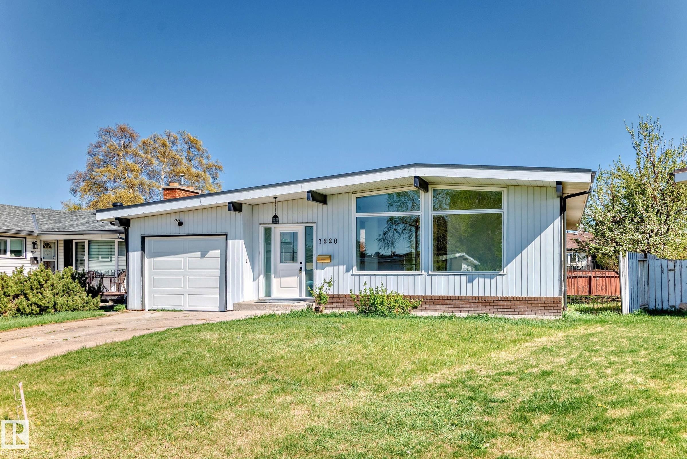 The property features a white exterior, a single-car garage, and large front windows - 7220 152A Ave, Edmonton, AB - Outdoor