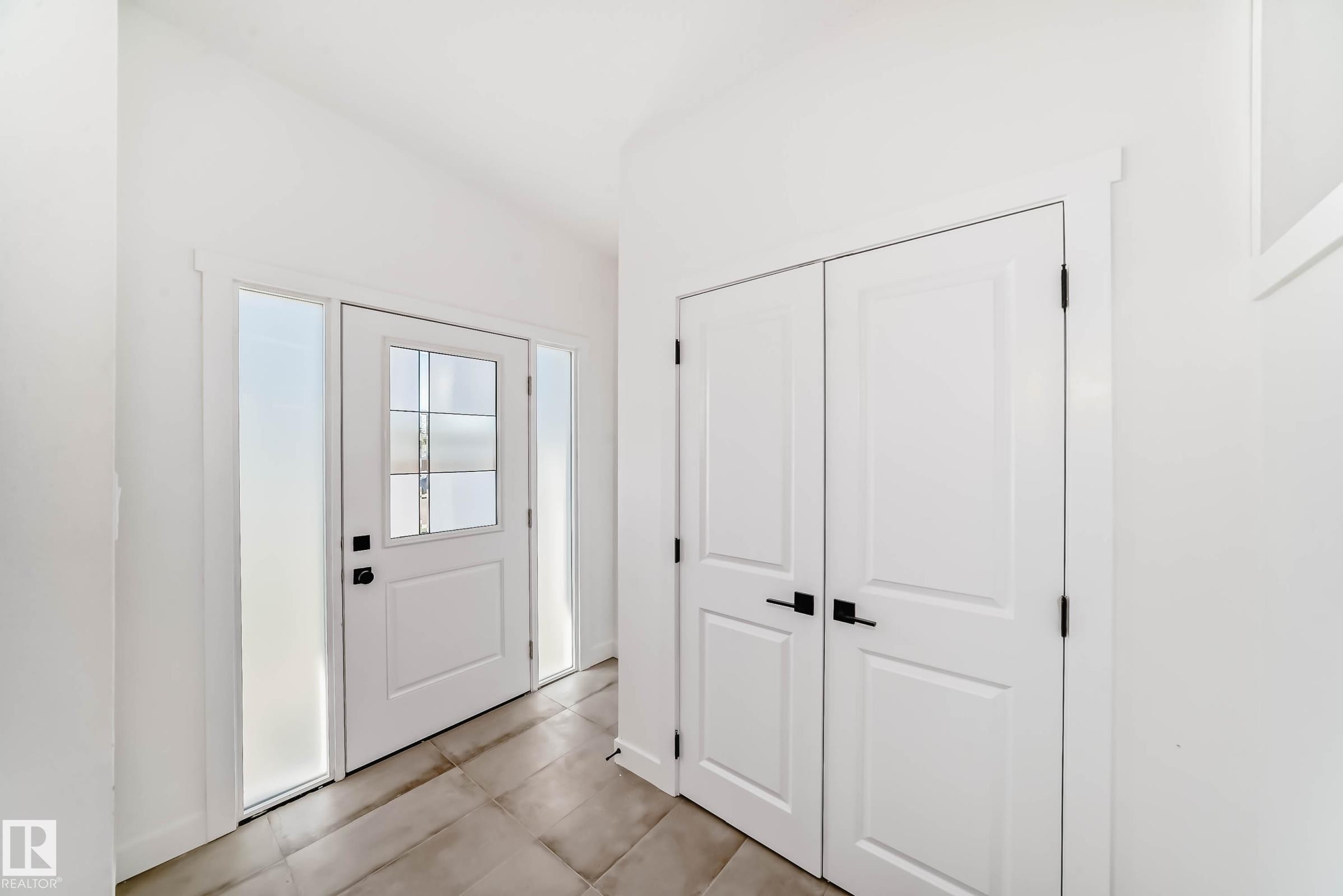 The property entrance features a white door with glass panels and side lights, complemented by large tile flooring and white panel doors - 7220 152A Ave, Edmonton, AB - Indoor Photo Showing Other Room