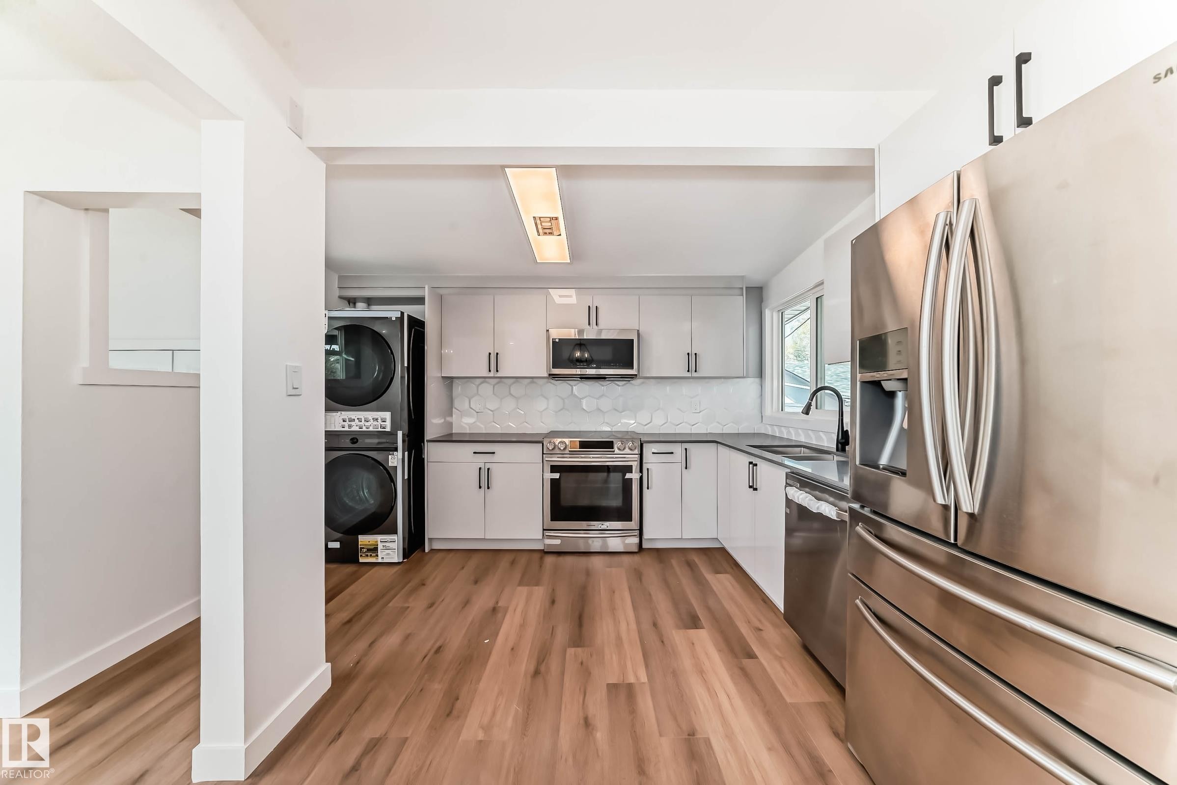 The kitchen features light-colored cabinetry, stainless steel appliances, and wood-style flooring - 7220 152A Ave, Edmonton, AB - Indoor Photo Showing Kitchen