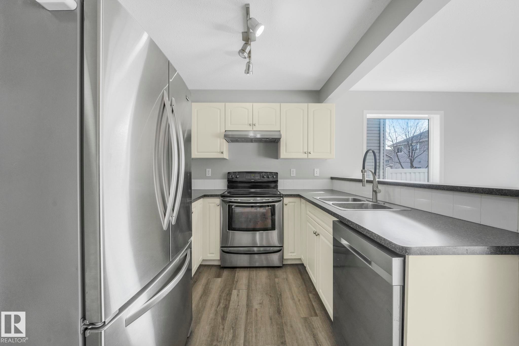The kitchen features stainless steel appliances, including a refrigerator, range, and dishwasher, along with a double basin sink and light-colored cabinetry - 123 230 Edwards Drive, Edmonton, AB - Indoor Photo Showing Kitchen With Stainless Steel Kitchen With Double Sink