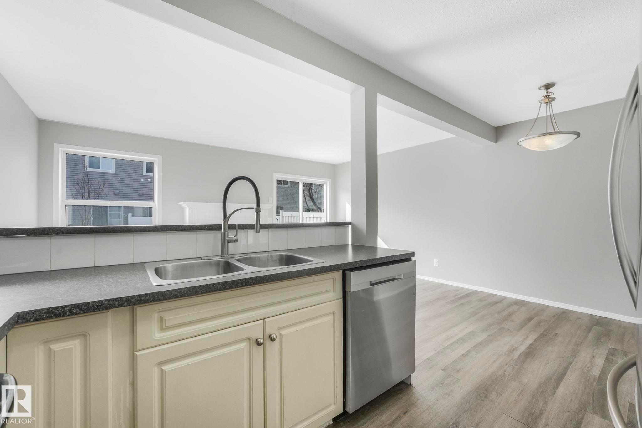 The kitchen features a double basin sink with a high-arc faucet, light-colored cabinetry, a dark countertop, and a stainless steel dishwasher - 123 230 Edwards Drive, Edmonton, AB - Indoor Photo Showing Kitchen With Double Sink