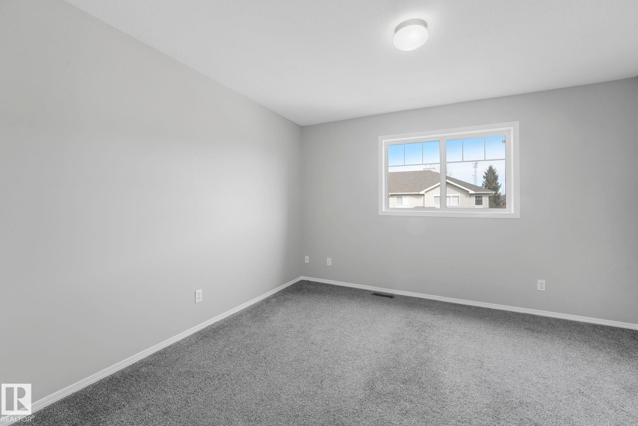 This room features light gray walls, gray carpeting, and a window with white trim providing natural light - 123 230 Edwards Drive, Edmonton, AB - Indoor Photo Showing Other Room