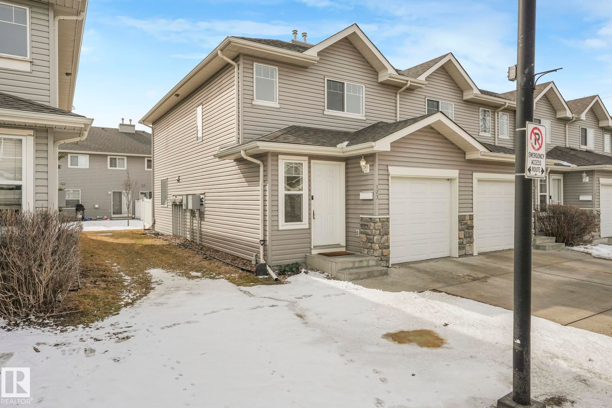 The property features light gray siding, a white front door, and an attached garage with a white door - 123 230 Edwards Drive, Edmonton, AB - Outdoor With Facade