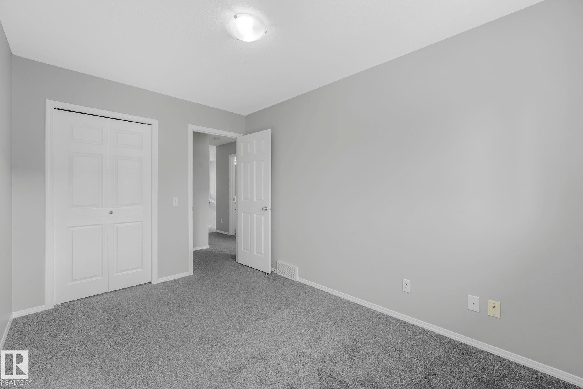 This room features light gray walls, gray carpeting, a ceiling-mounted light fixture, and white bi-fold closet doors - 123 230 Edwards Drive, Edmonton, AB - Indoor Photo Showing Other Room
