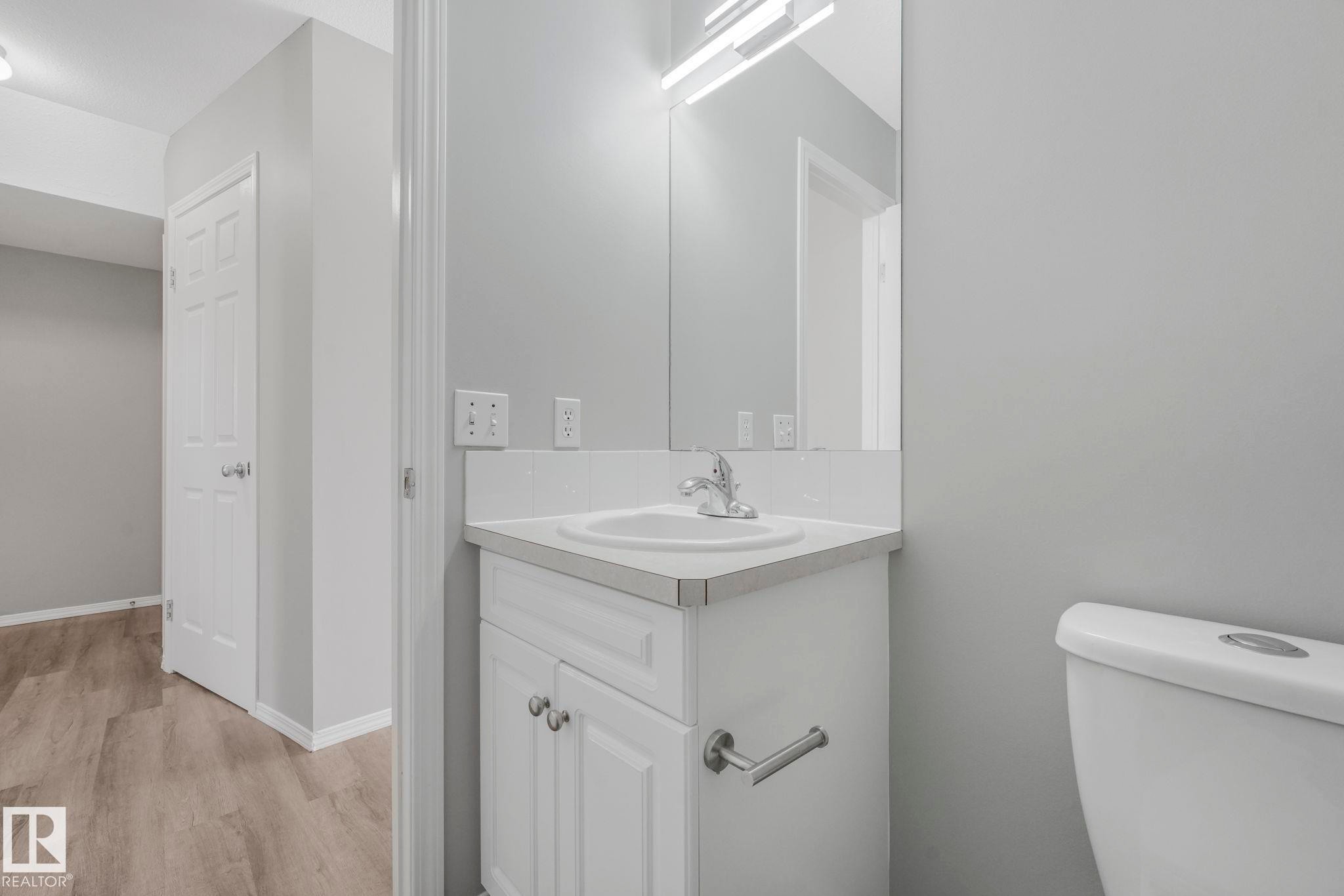 Bathroom with a white vanity and integrated sink, a mirror with overhead lighting, and light gray walls - 123 230 Edwards Drive, Edmonton, AB - Indoor Photo Showing Bathroom
