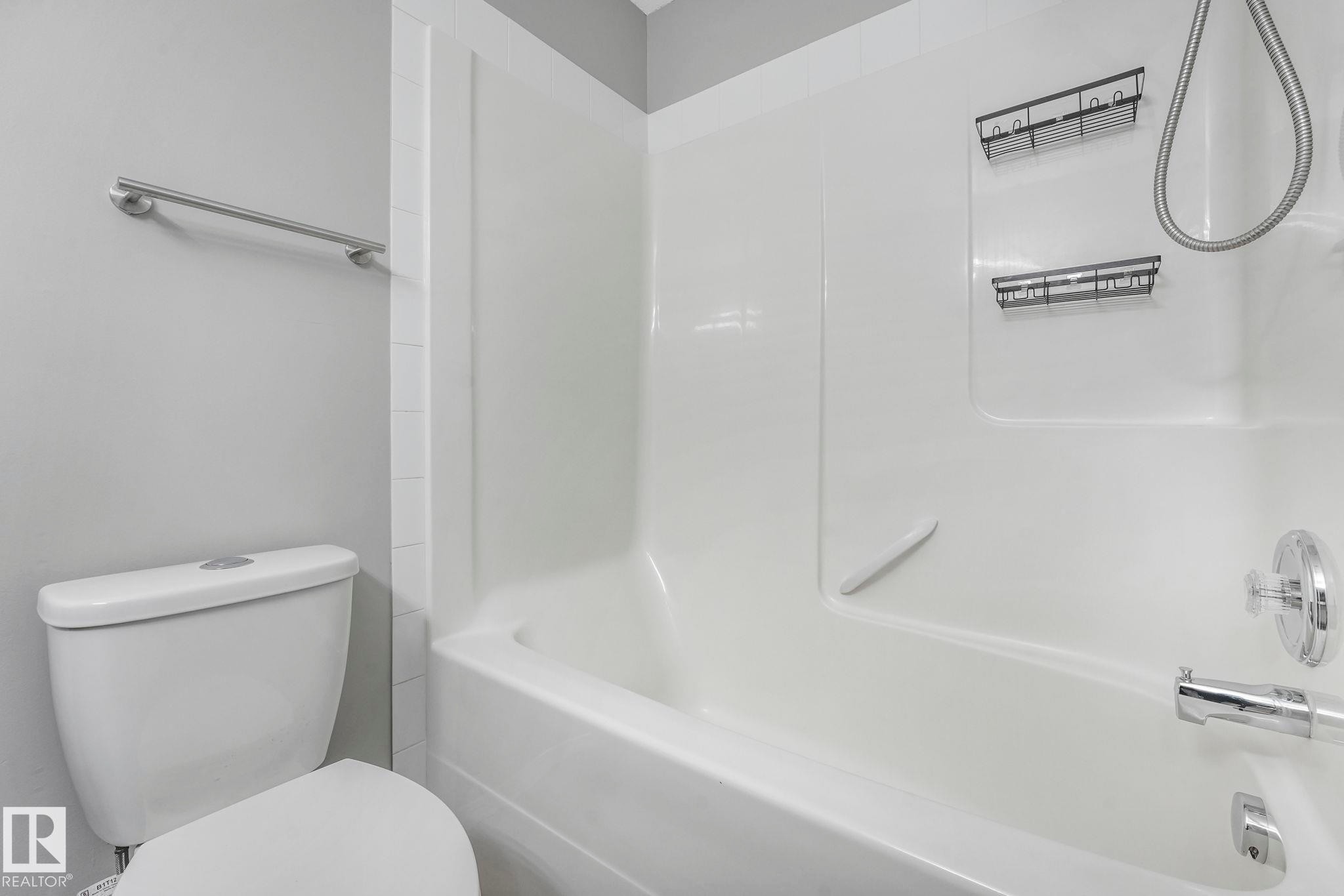 Bathroom featuring a white toilet, a white shower and bath unit, and a chrome towel bar - 123 230 Edwards Drive, Edmonton, AB - Indoor Photo Showing Bathroom