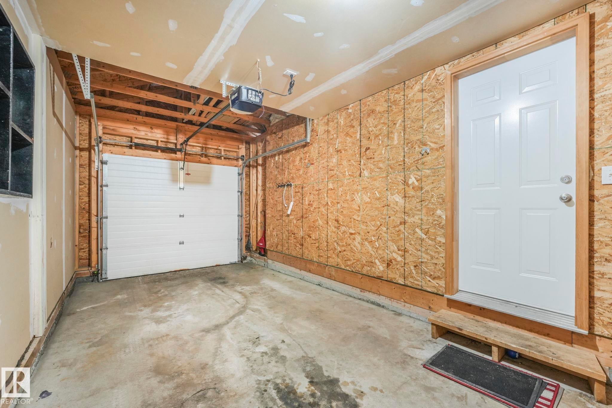 The property features a garage with a concrete floor, an overhead garage door, and visible wooden framing - 123 230 Edwards Drive, Edmonton, AB - Indoor Photo Showing Garage