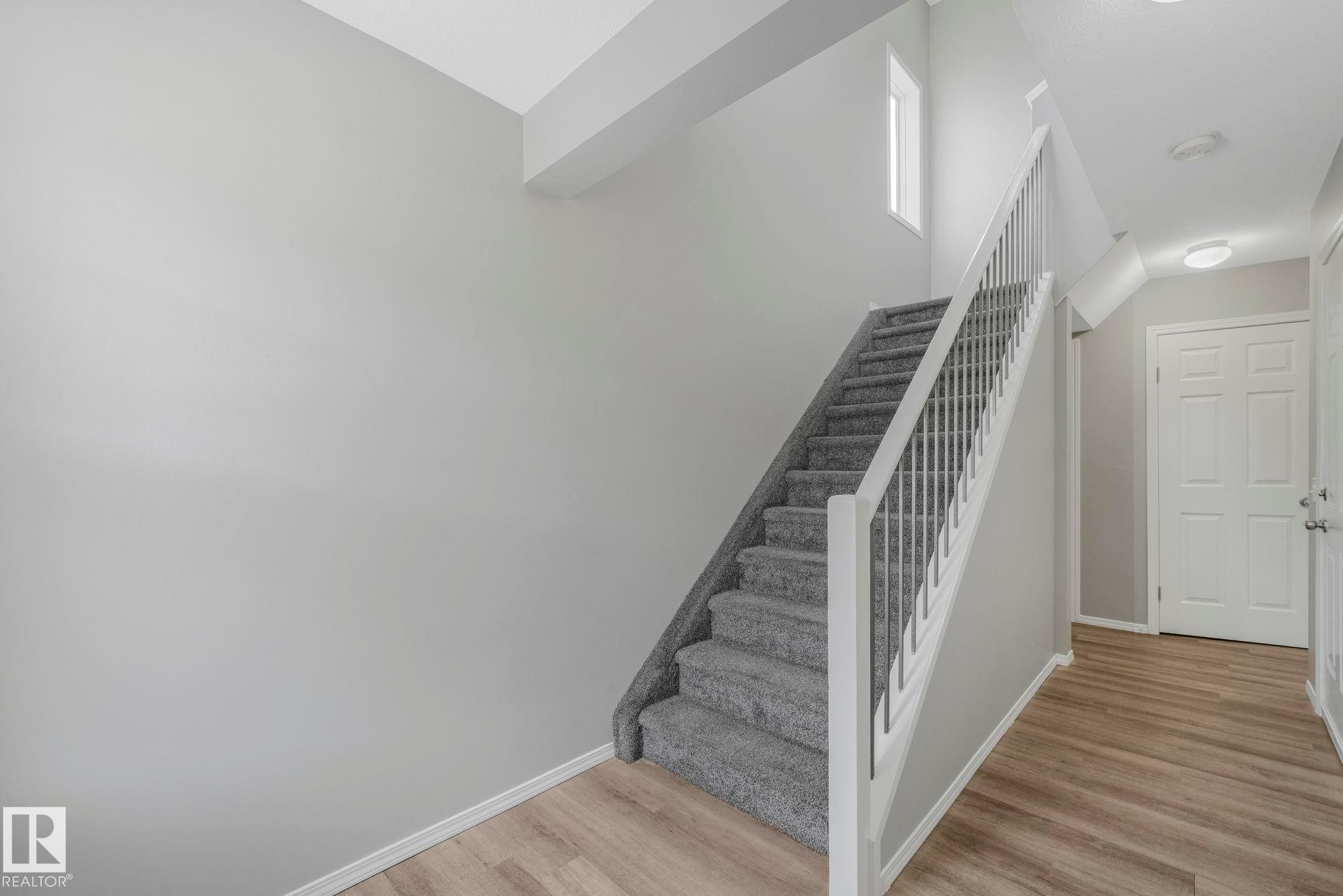 The property features a staircase with carpeted steps and white railings, a front door with white panels, and light wood flooring in the entryway - 123 230 Edwards Drive, Edmonton, AB - Indoor Photo Showing Other Room