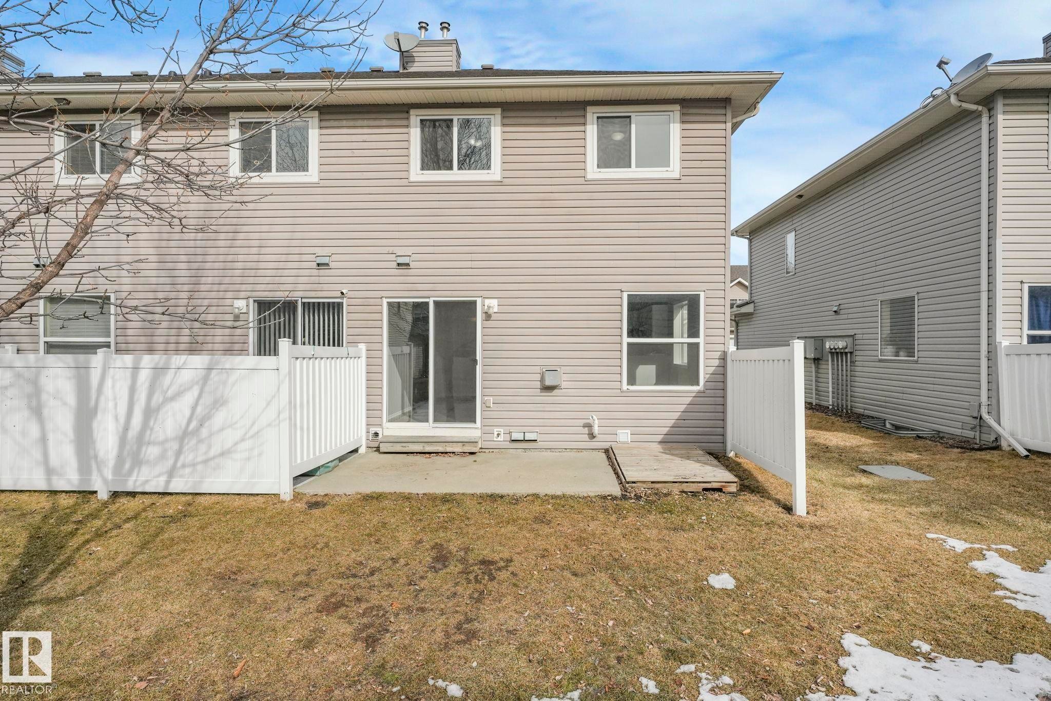 The property features a concrete patio and a fenced yard with a partially visible tree - 123 230 Edwards Drive, Edmonton, AB - Outdoor With Exterior