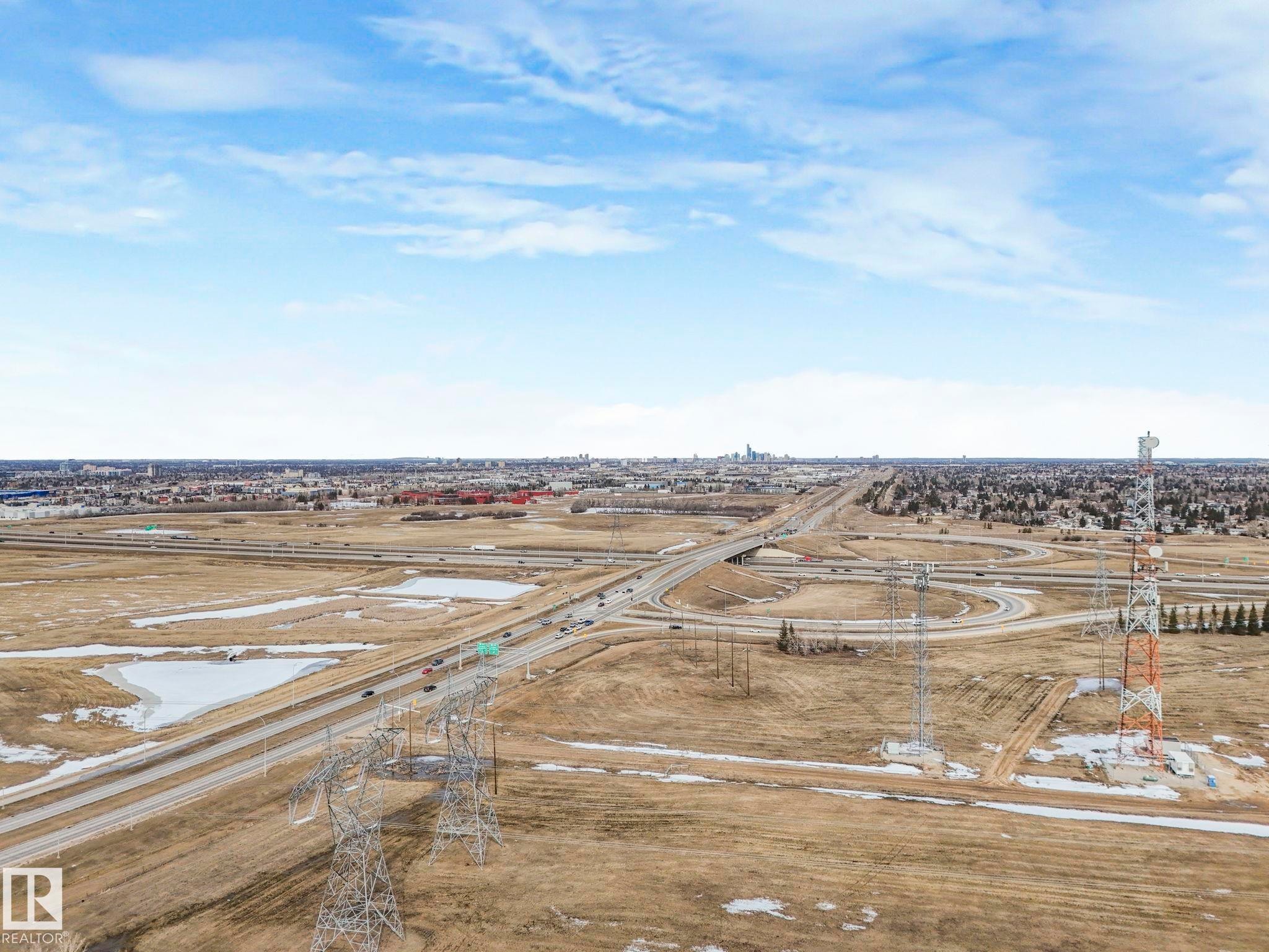 Aerial view showcasing the expansive surrounding area with highways, commercial buildings, and open fields under a blue sky - 123 230 Edwards Drive, Edmonton, AB - Outdoor With View