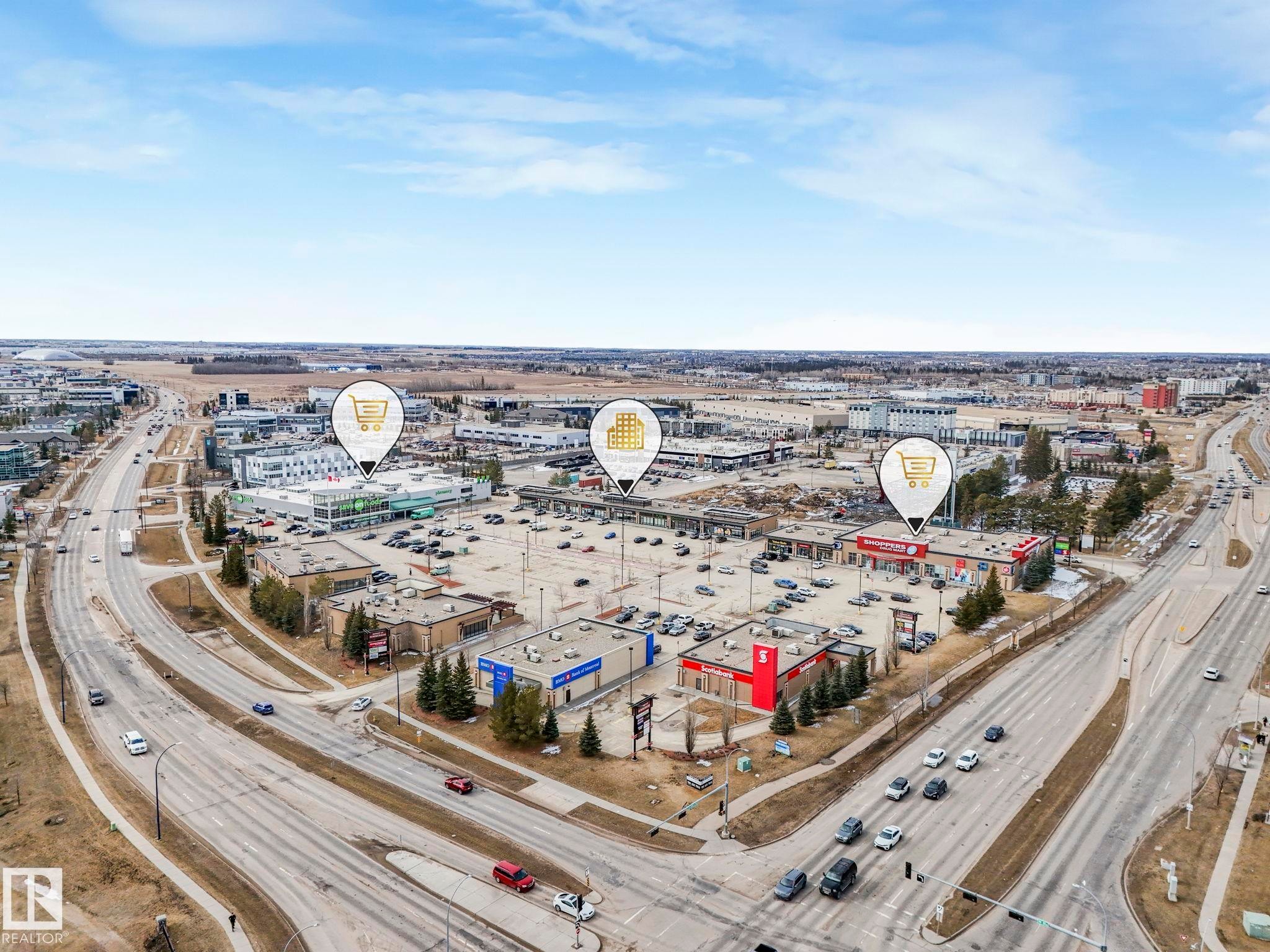 The property is located within a vibrant commercial area, featuring several retail buildings and ample parking - 123 230 Edwards Drive, Edmonton, AB - Outdoor With View
