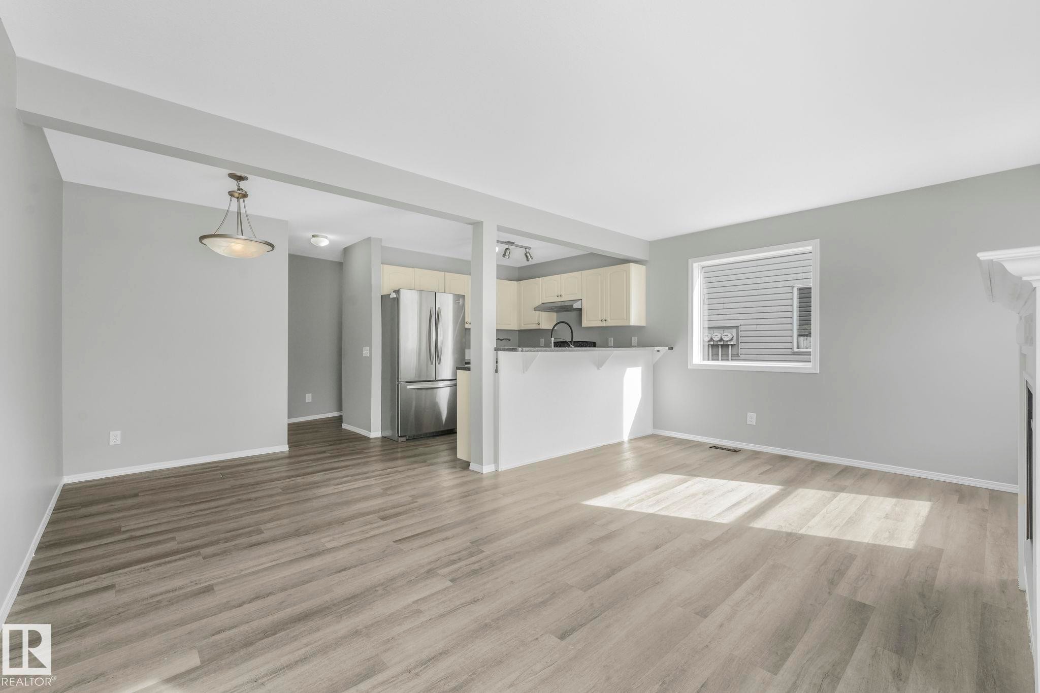 The property features light-colored flooring, a kitchen with a stainless steel refrigerator, and a window providing natural light - 123 230 Edwards Drive, Edmonton, AB - Indoor Photo Showing Other Room