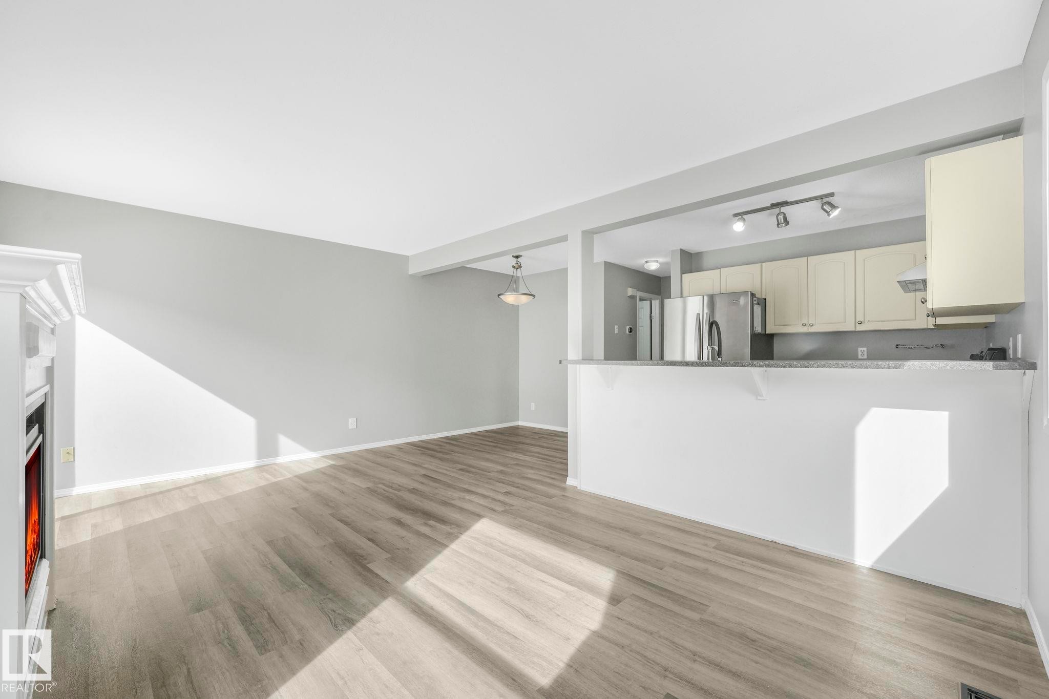 Open concept living area featuring light gray walls and wood-look flooring - 123 230 Edwards Drive, Edmonton, AB - Indoor Photo Showing Kitchen