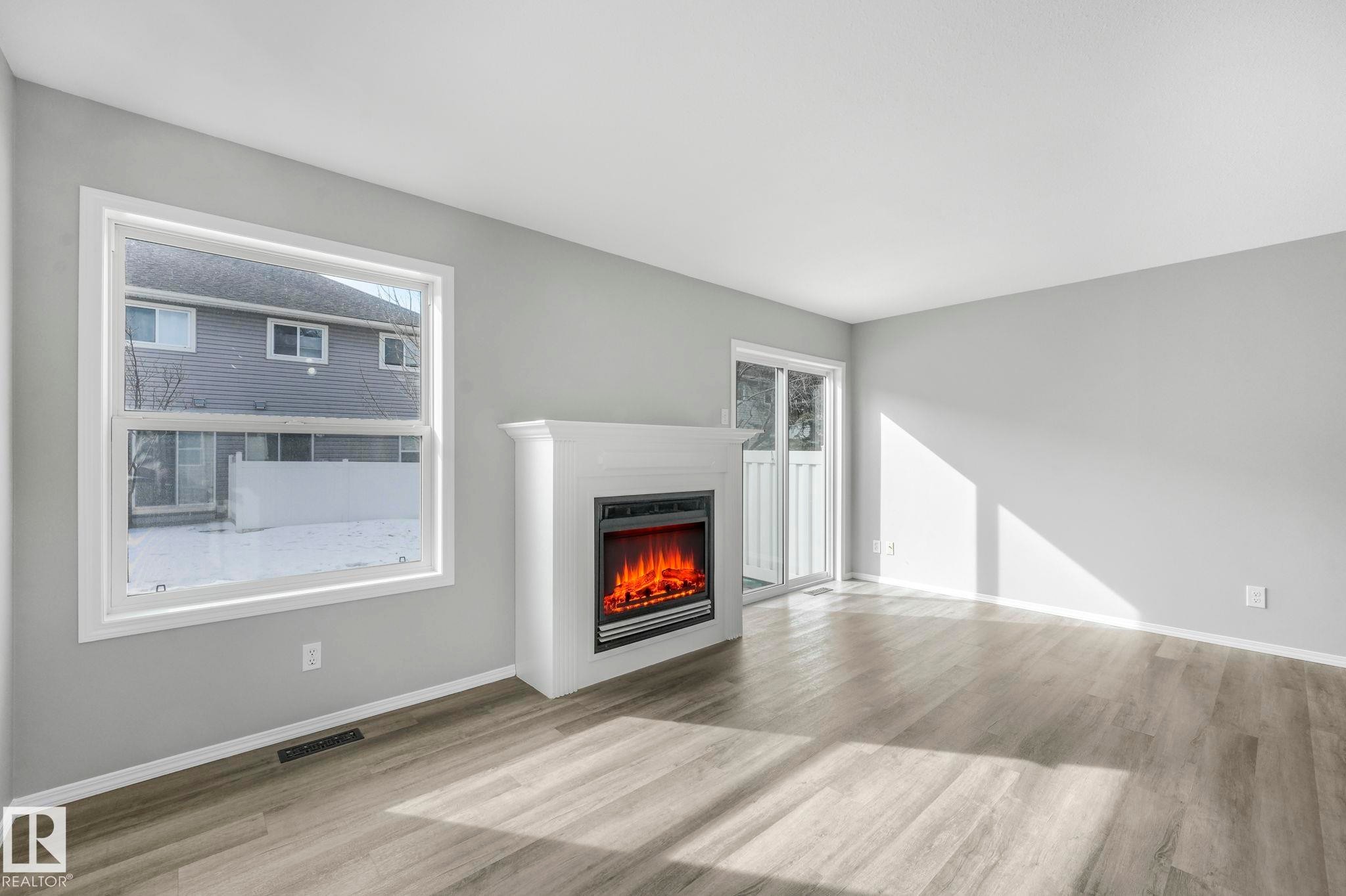 Living space featuring light-colored flooring, a white fireplace with an electric insert, and a sliding glass door leading to the outside - 123 230 Edwards Drive, Edmonton, AB - Indoor Photo Showing Living Room With Fireplace