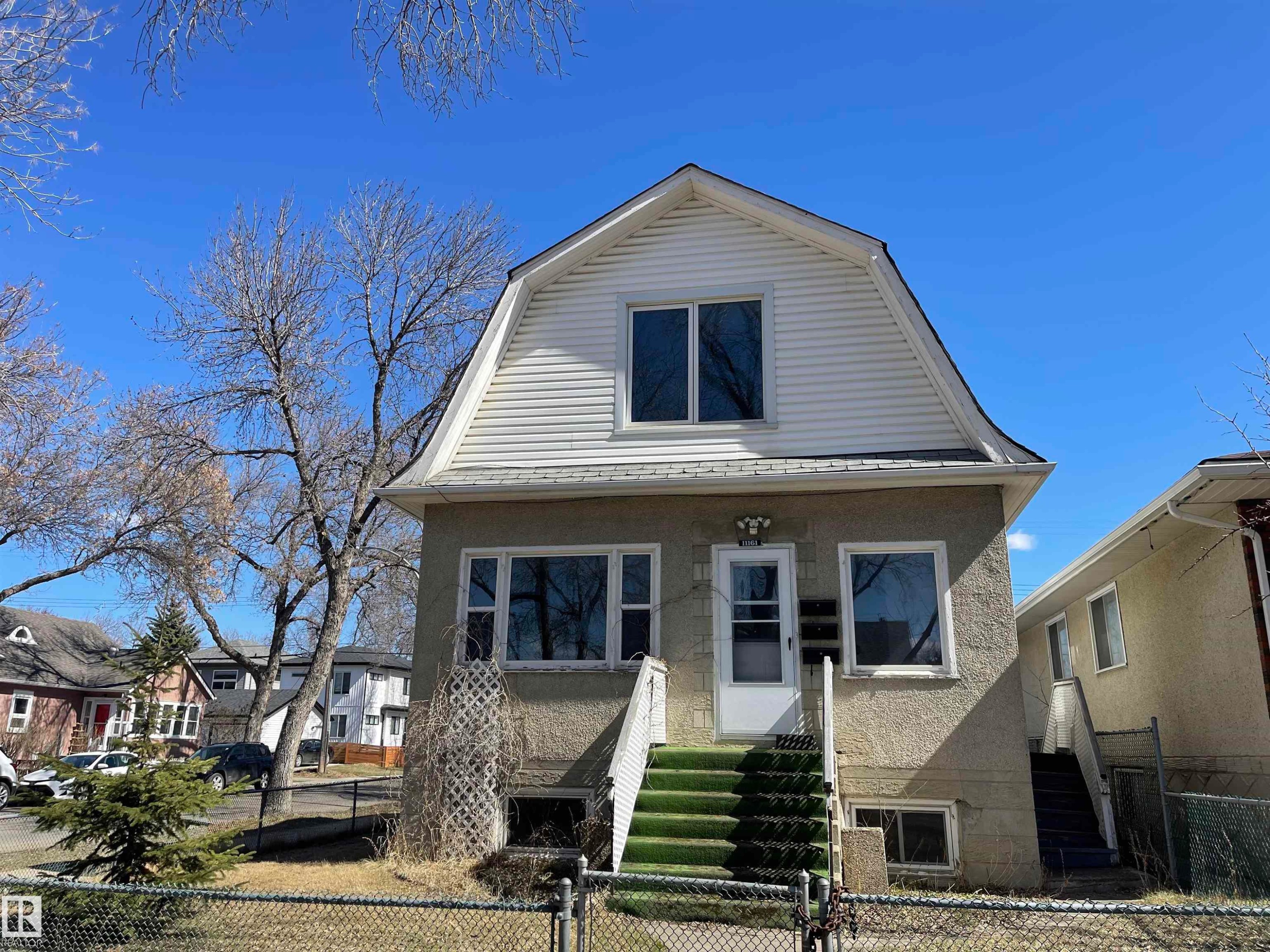 This property features a distinct gambrel roofline with white siding on the upper level - 11161 96 Street, Edmonton, AB - Outdoor With Facade