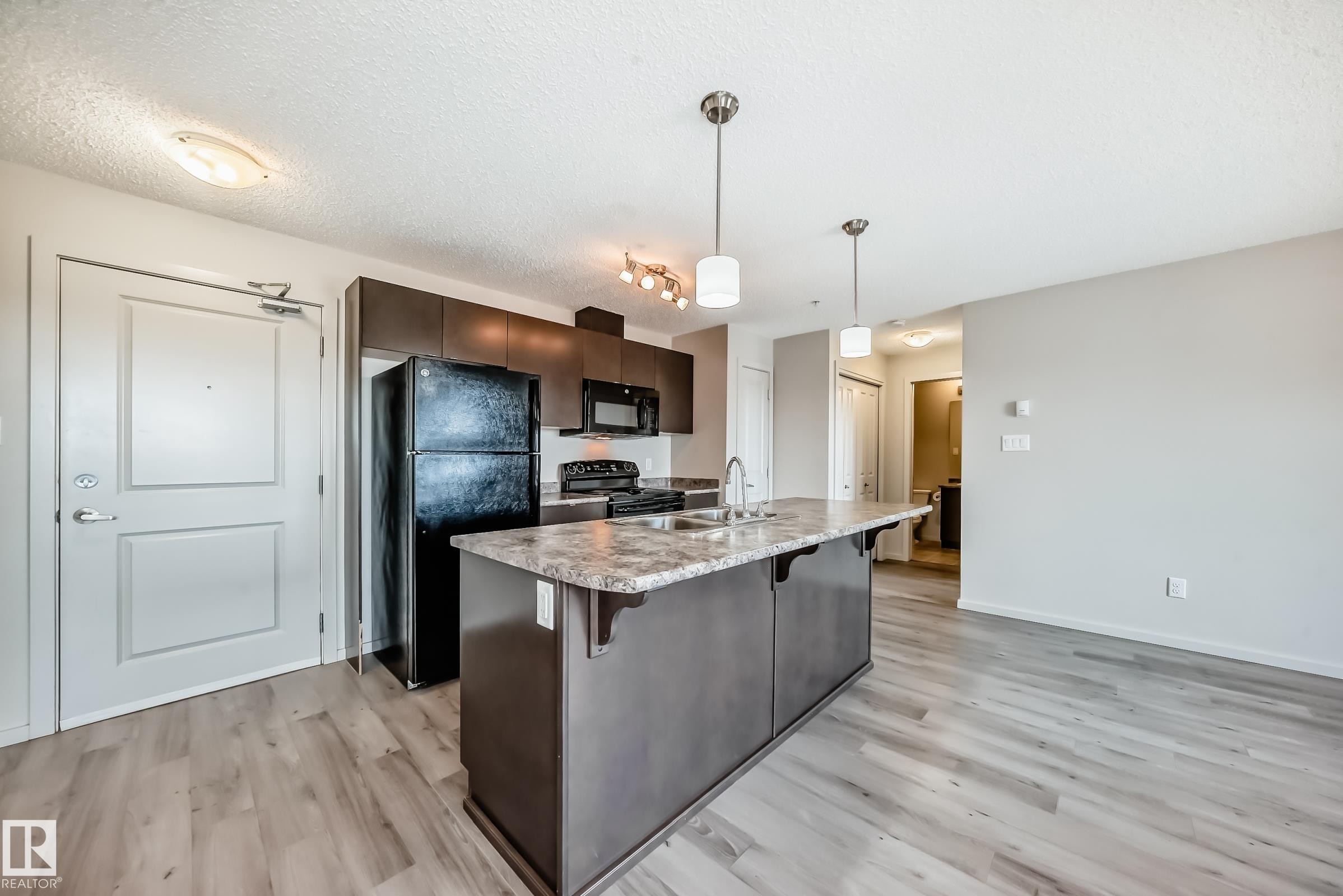 The kitchen features dark wood cabinetry, a black refrigerator, a black oven, and a kitchen island with a sink and pendant lighting - 332 344 Windermere Road, Edmonton, AB - Indoor Photo Showing Kitchen With Double Sink