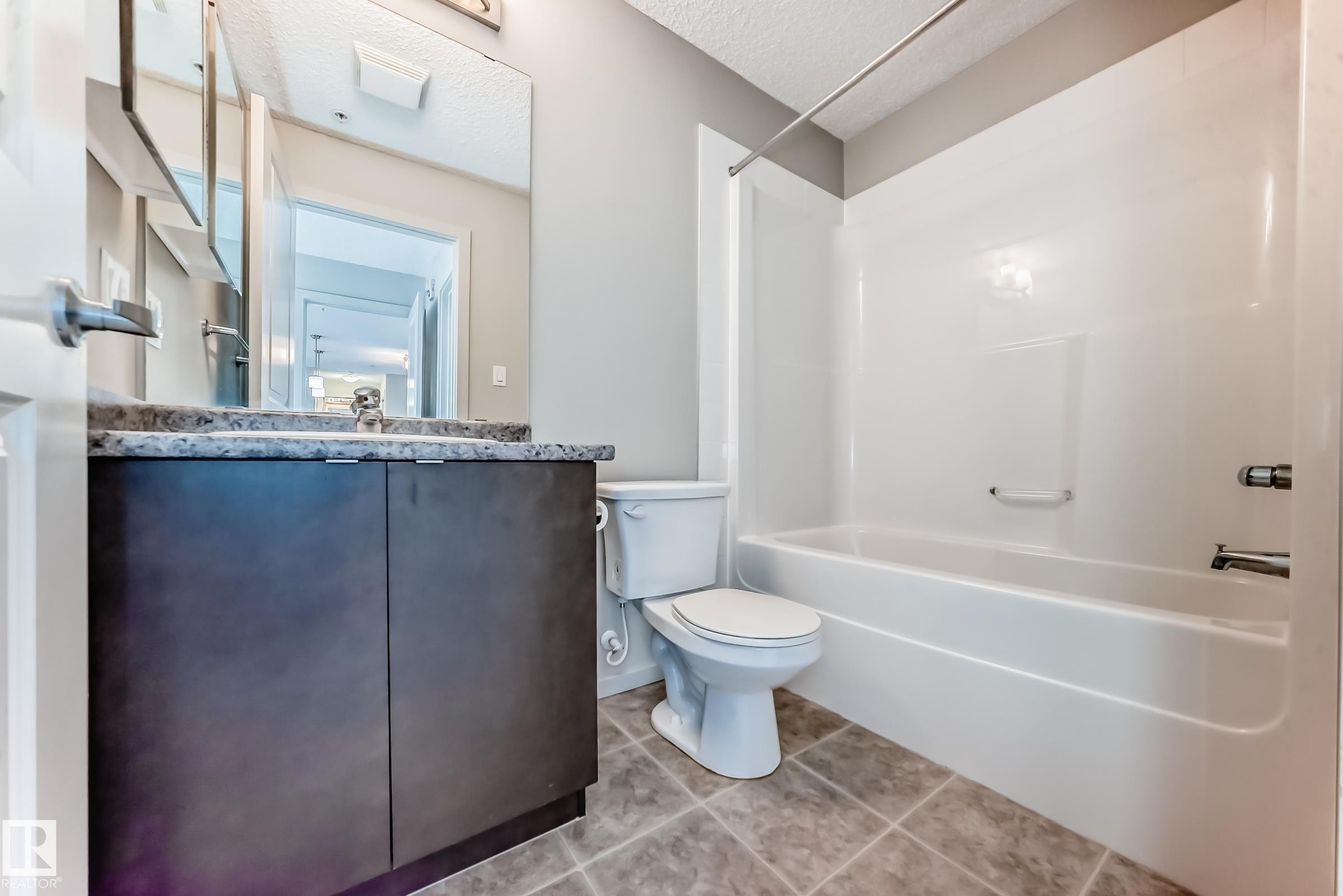 Bathroom featuring a dark wood vanity with a light-colored countertop, a white toilet, and a white bathtub with a shower - 332 344 Windermere Road, Edmonton, AB - Indoor Photo Showing Bathroom
