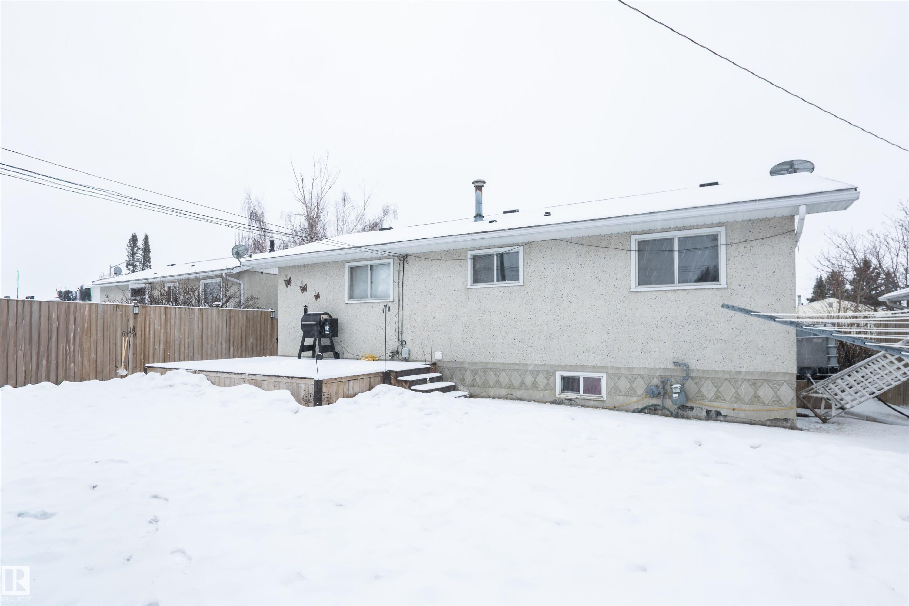 The property features a backyard with a wooden fence and a raised wooden deck - 4420 56 Avenue, Barrhead, AB - Outdoor