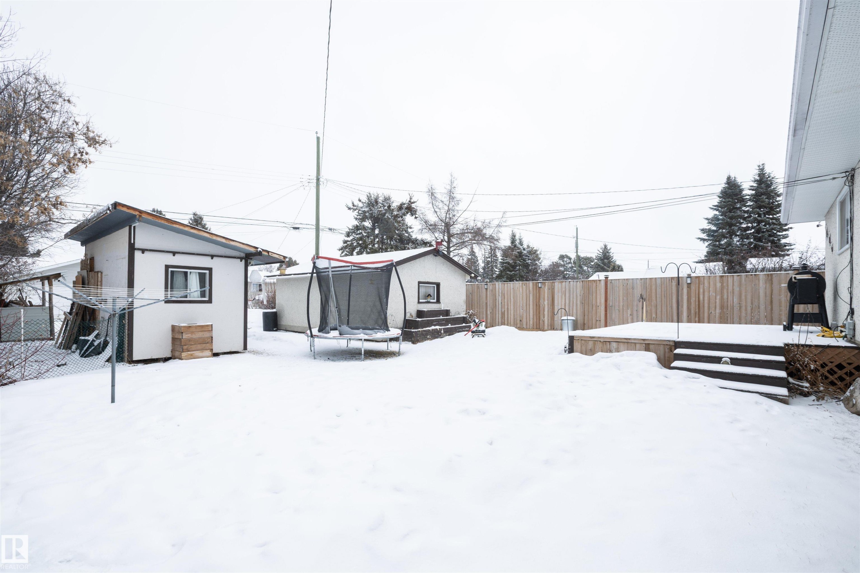 The property features a spacious yard with a deck and includes two sheds - 4420 56 Avenue, Barrhead, AB - Outdoor