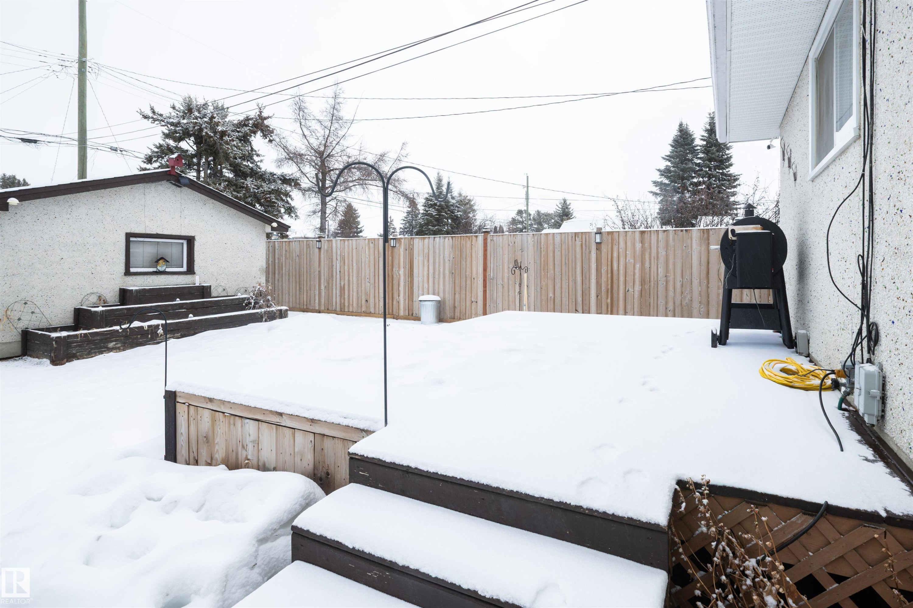 The property features a wooden deck with steps, a fenced yard, and an exterior building with a window - 4420 56 Avenue, Barrhead, AB - Outdoor