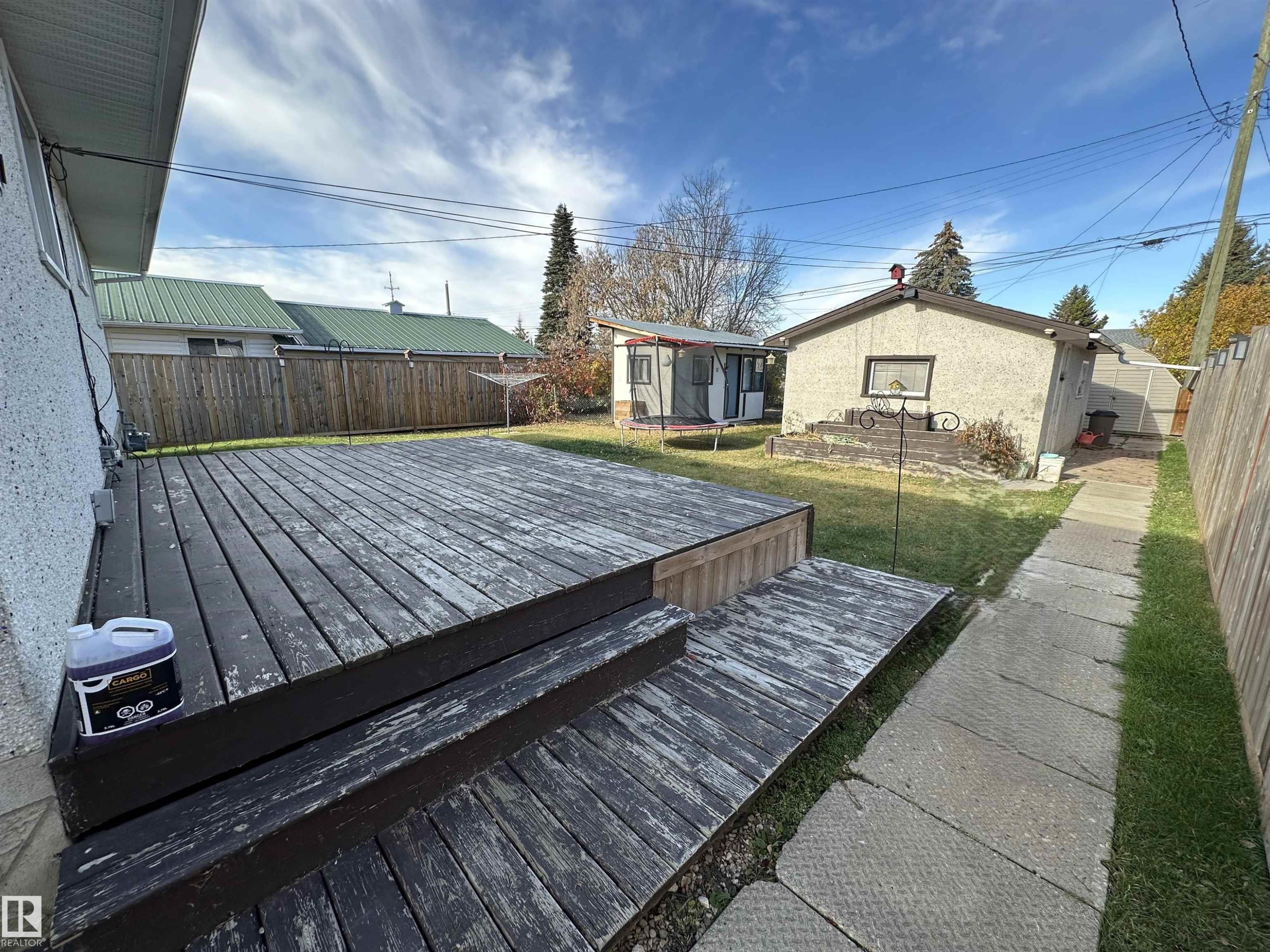 The property features a wooden deck with steps, a concrete pathway, and a fenced yard - 4420 56 Avenue, Barrhead, AB - Outdoor With Deck Patio Veranda