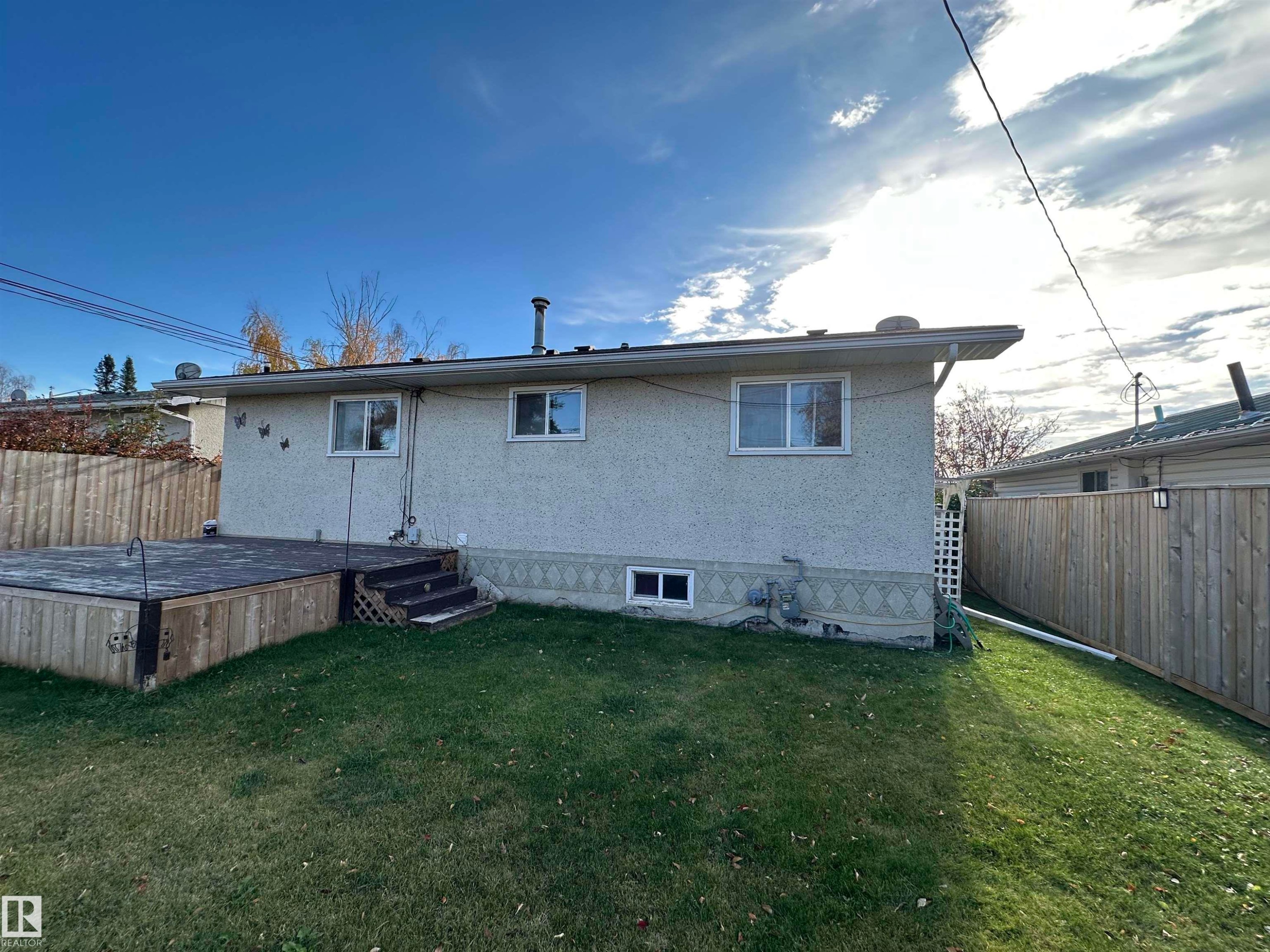 The property features a backyard with a wooden deck and steps, a lawn, and a light-colored exterior with windows - 4420 56 Avenue, Barrhead, AB - Outdoor