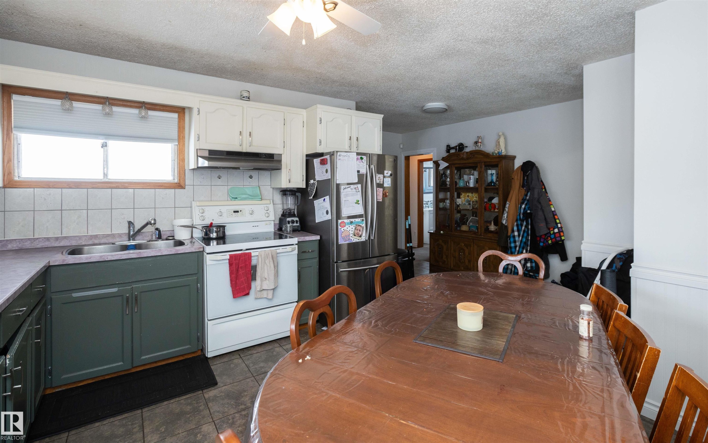 The kitchen and dining area features tile flooring, white upper cabinetry, and a double basin sink - 4420 56 Avenue, Barrhead, AB - Indoor