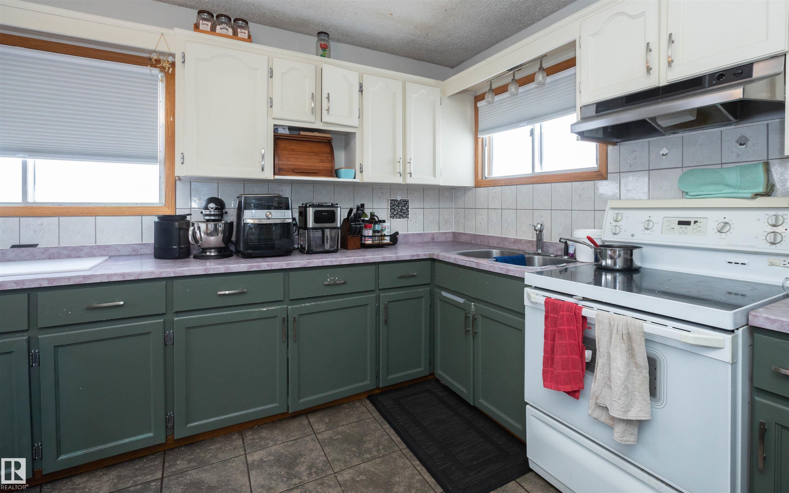 The kitchen features two-toned cabinetry, light countertops, a tile backsplash, and a white electric range - 4420 56 Avenue, Barrhead, AB - Indoor Photo Showing Kitchen With Double Sink