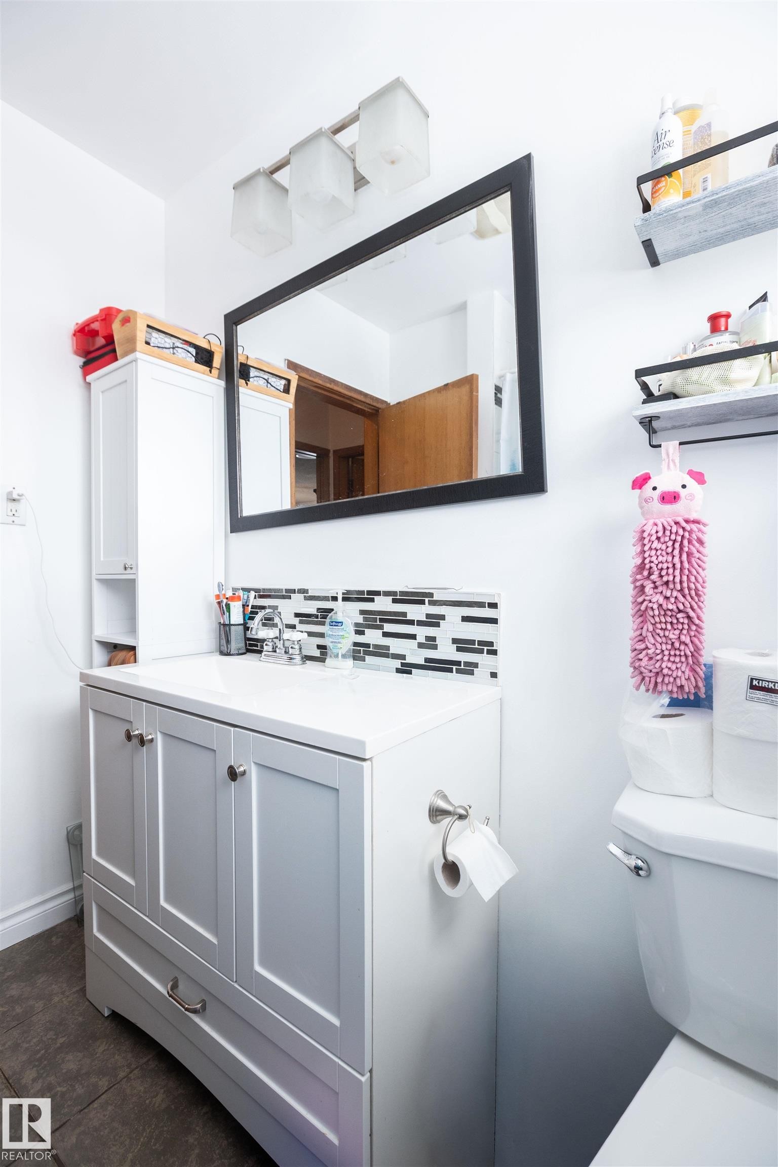 The bathroom features a vanity with a white countertop, a rectangular mirror with a black frame, and a three-light fixture above the mirror - 4420 56 Avenue, Barrhead, AB - Indoor Photo Showing Bathroom