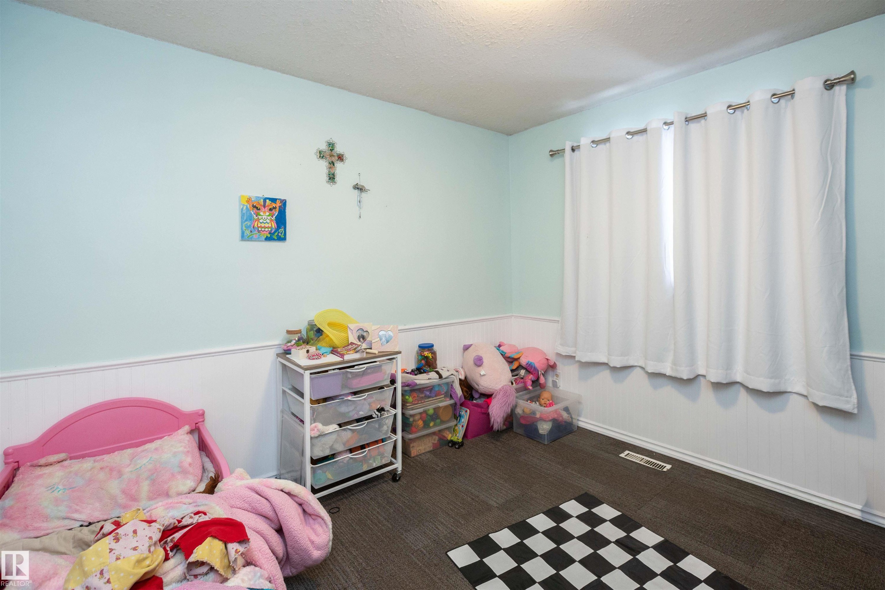 The room features light blue walls with white wainscoting, dark flooring, and a window with white curtains - 4420 56 Avenue, Barrhead, AB - Indoor Photo Showing Bedroom
