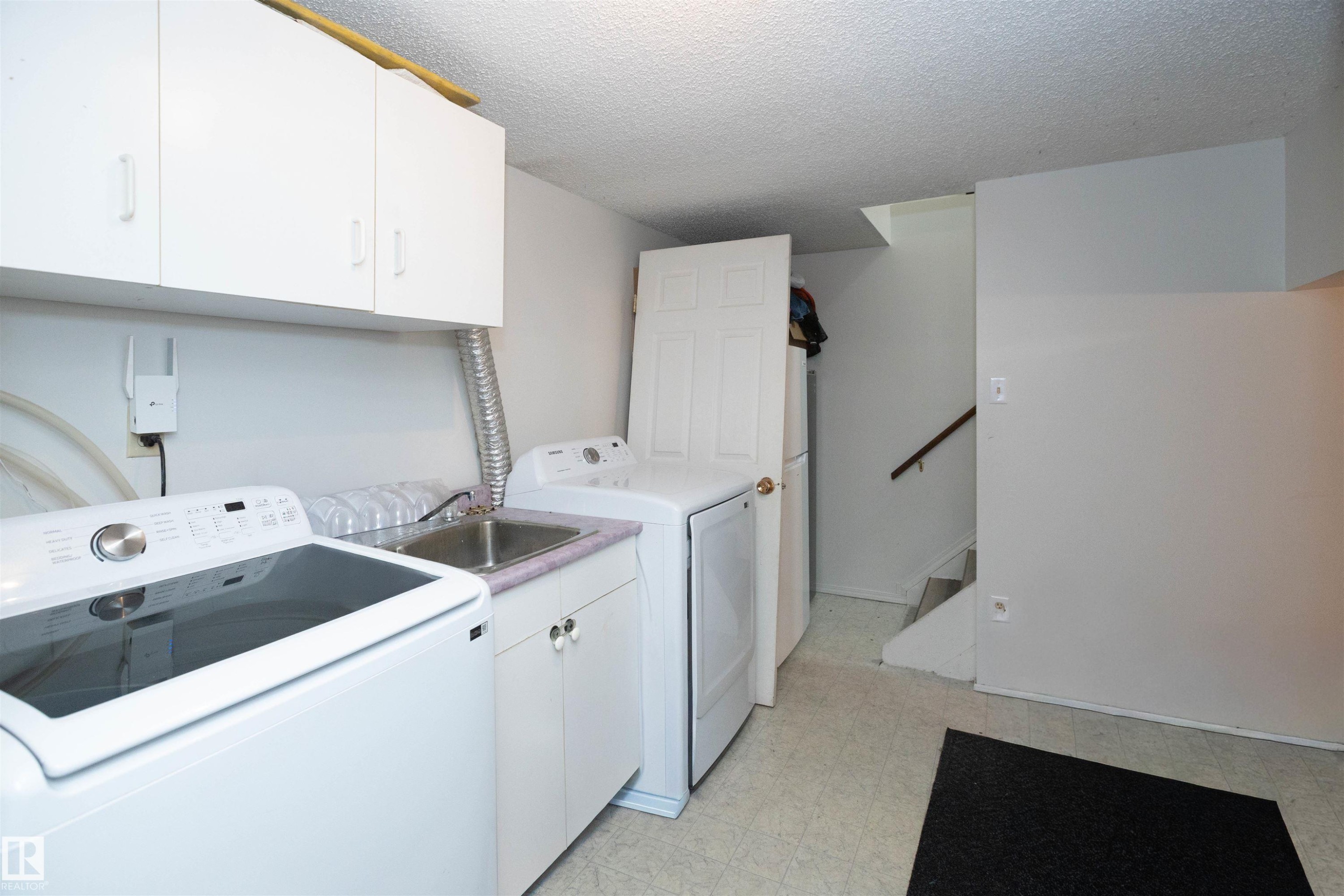 The property features a laundry area with a sink, white cabinetry, and a washer and dryer - 4420 56 Avenue, Barrhead, AB - Indoor Photo Showing Laundry Room