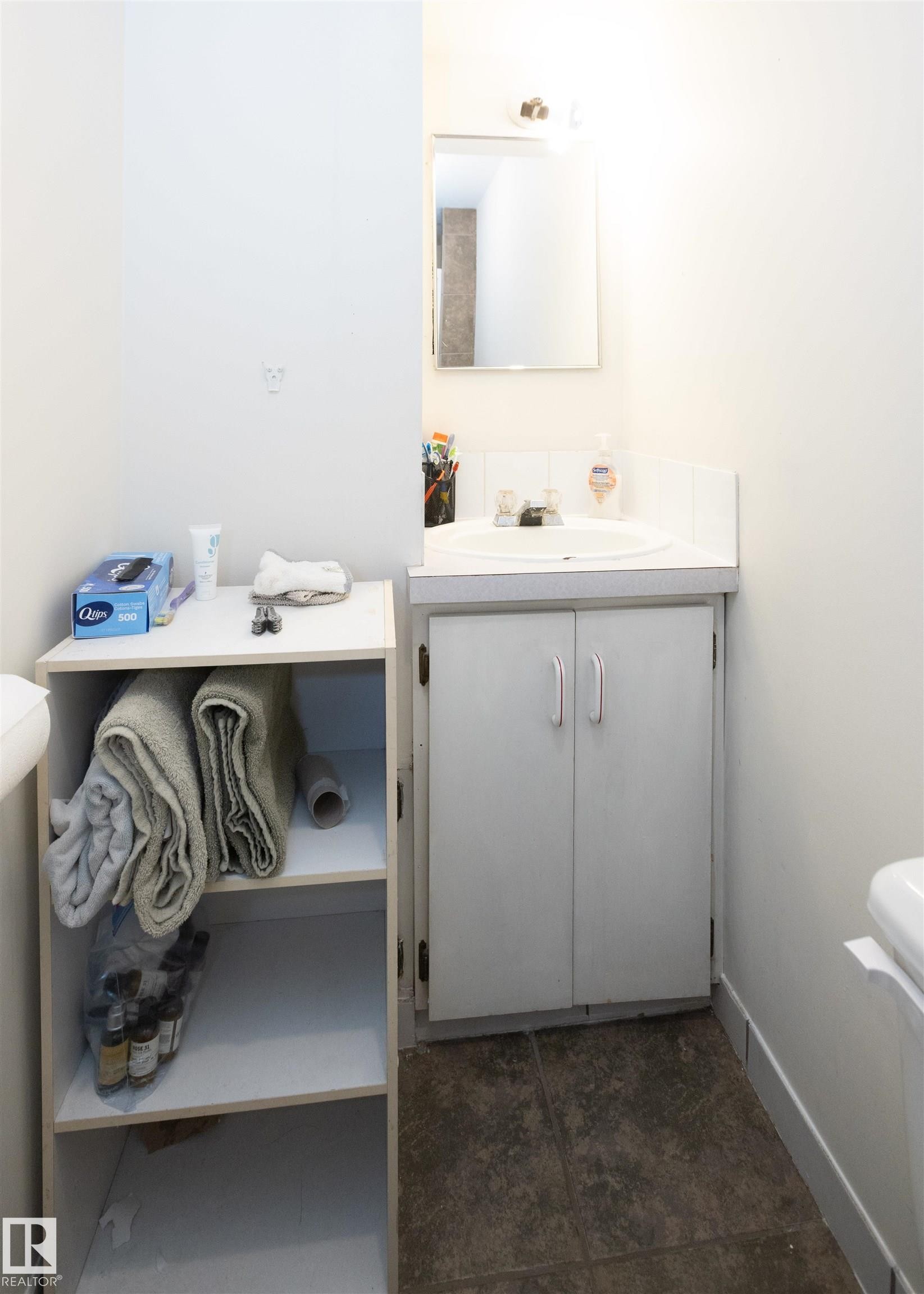 Bathroom featuring a vanity with an integrated sink and cabinet storage, a wall-mounted mirror, and tile flooring - 4420 56 Avenue, Barrhead, AB - Indoor Photo Showing Bathroom