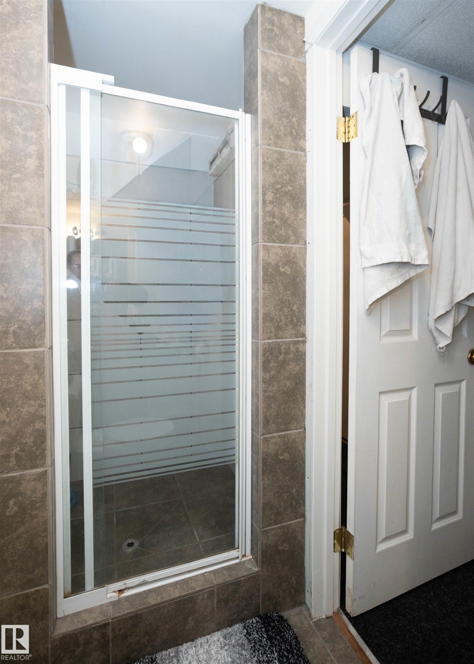 The bathroom features a shower enclosure with a sliding glass door and tiled walls - 4420 56 Avenue, Barrhead, AB - Indoor Photo Showing Bathroom