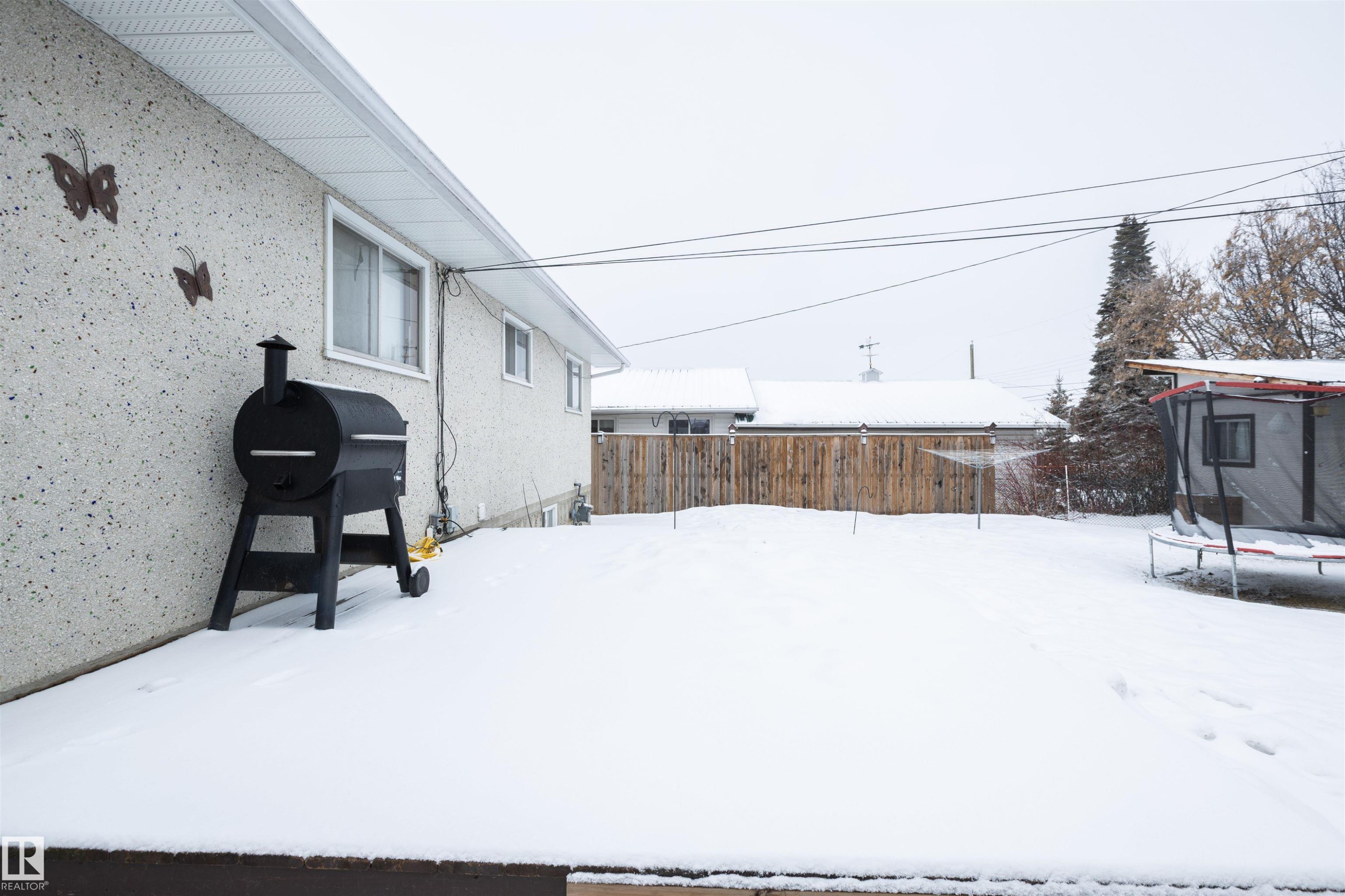 The property features a spacious backyard with a wooden fence and mature trees - 4420 56 Avenue, Barrhead, AB - Outdoor