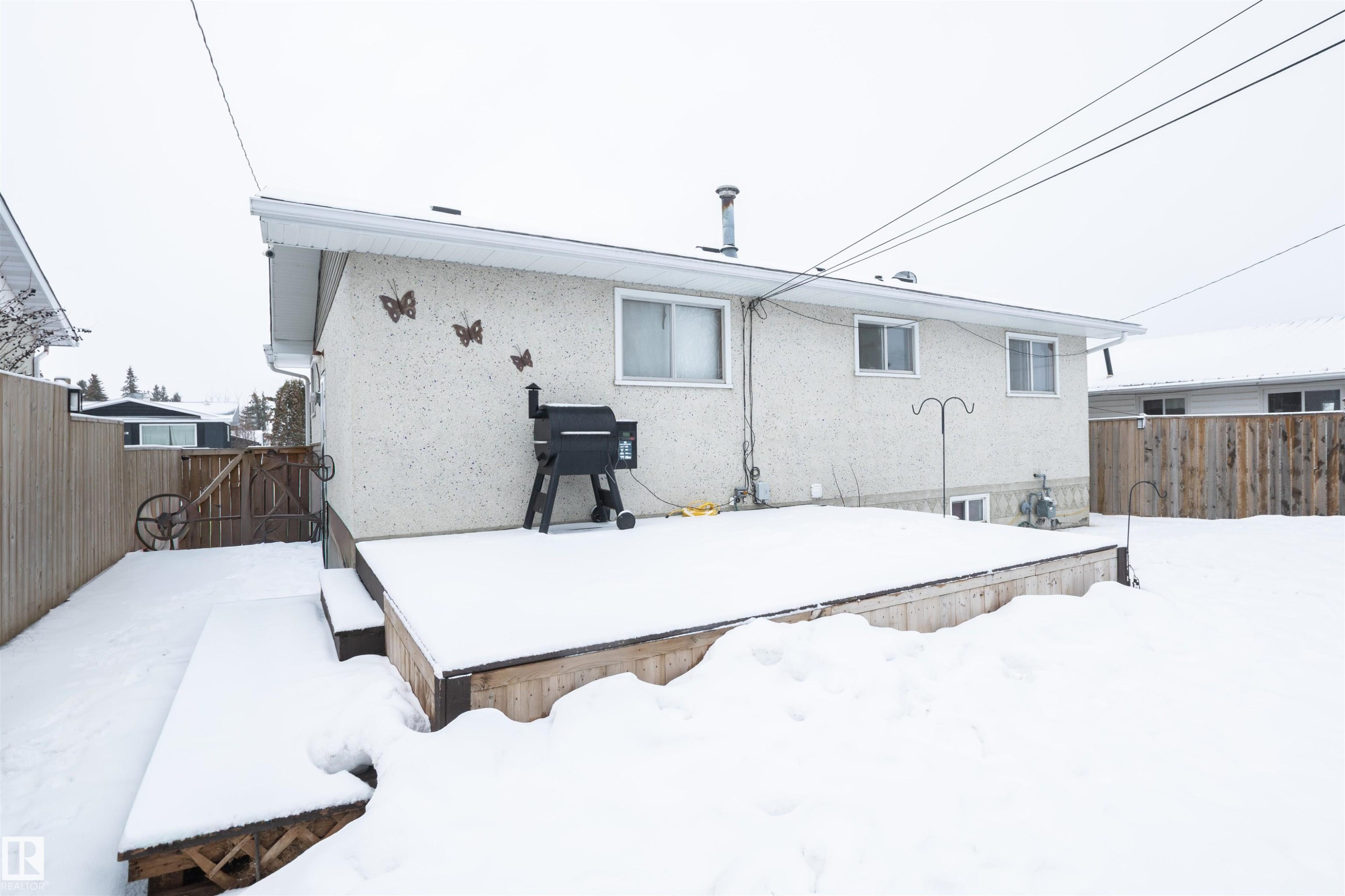 The property features a rear exterior with a stucco finish and a wooden deck - 4420 56 Avenue, Barrhead, AB - Outdoor With Exterior
