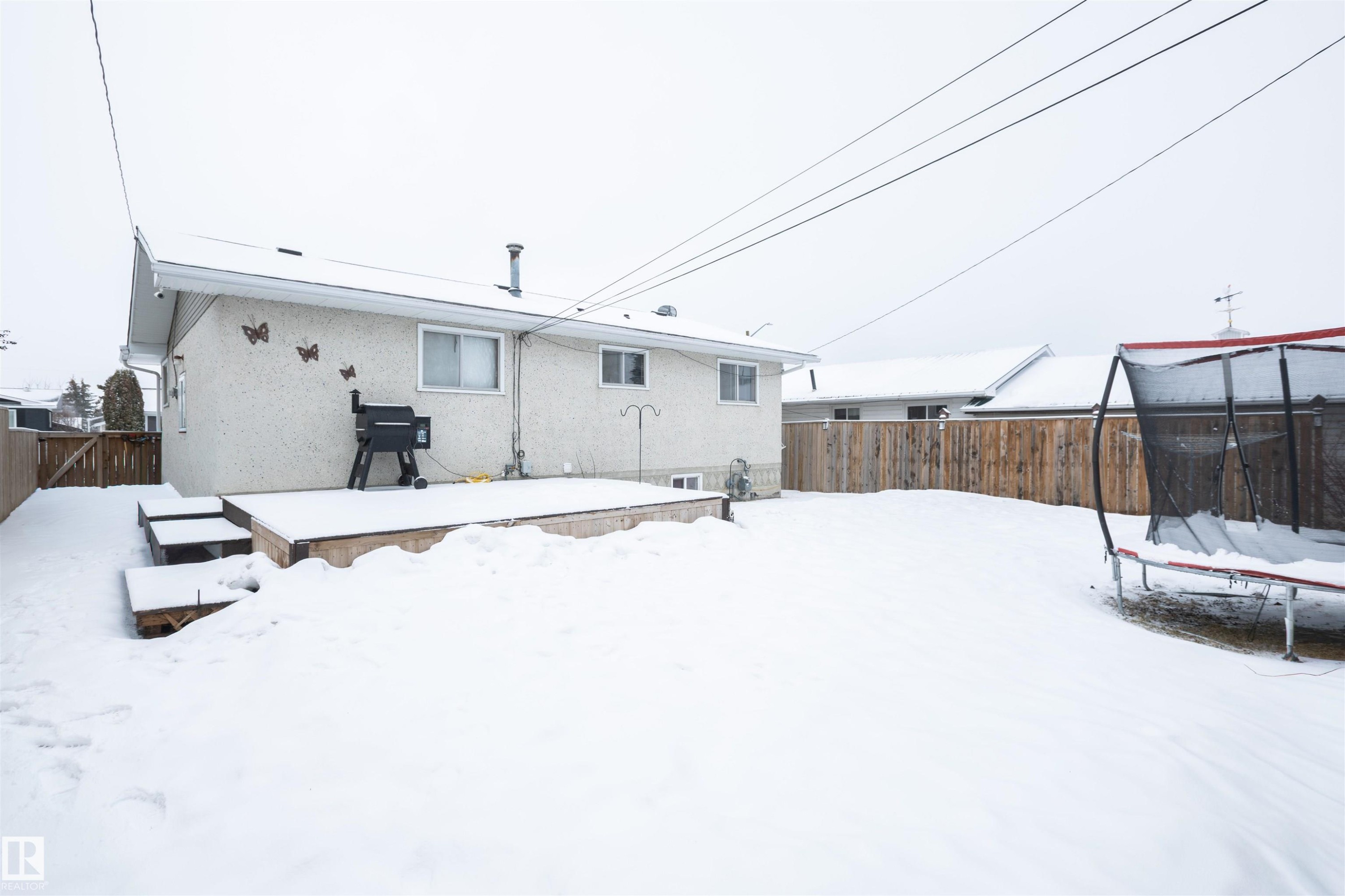The property features an exterior deck with steps, a fenced yard, and a stucco exterior - 4420 56 Avenue, Barrhead, AB - Outdoor