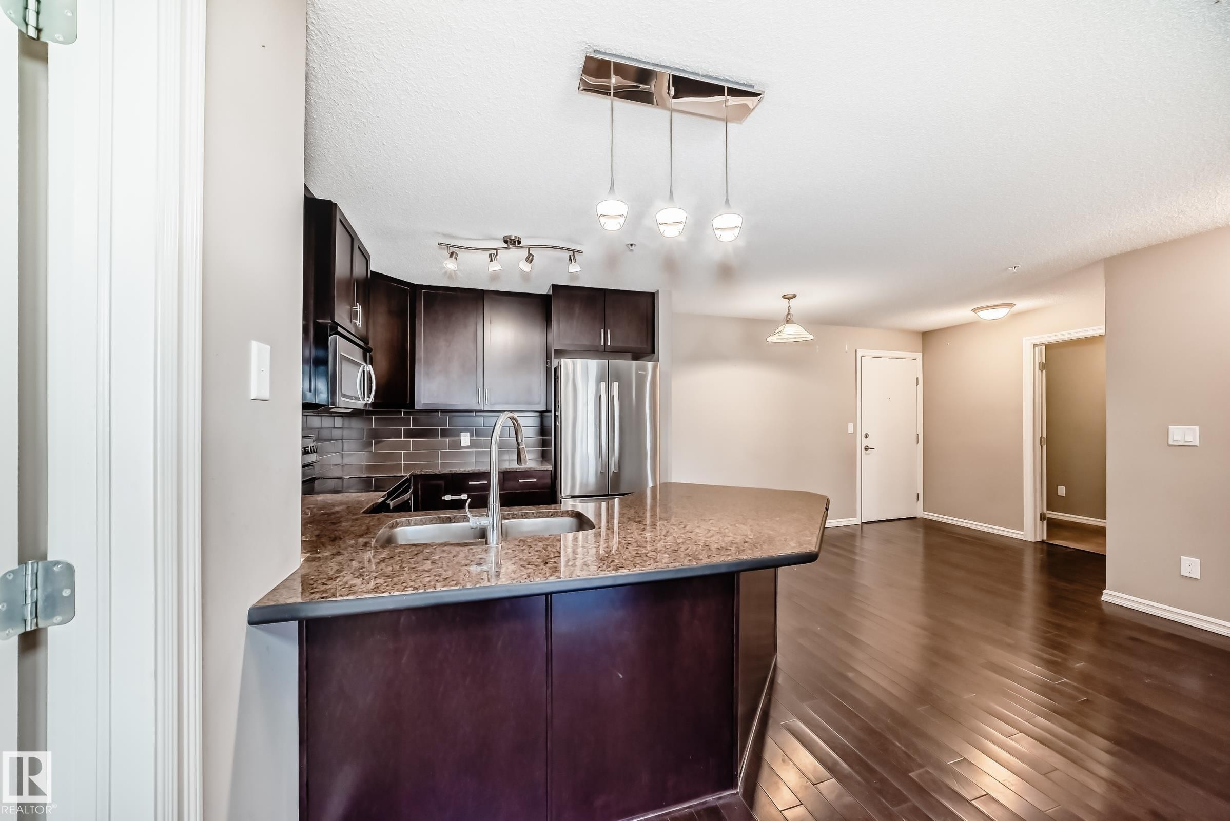 Open concept kitchen and living area featuring dark wood flooring, dark cabinetry, and stainless steel appliances - 208 2204 44 Ave, Edmonton, AB - Indoor Photo Showing Kitchen With Double Sink