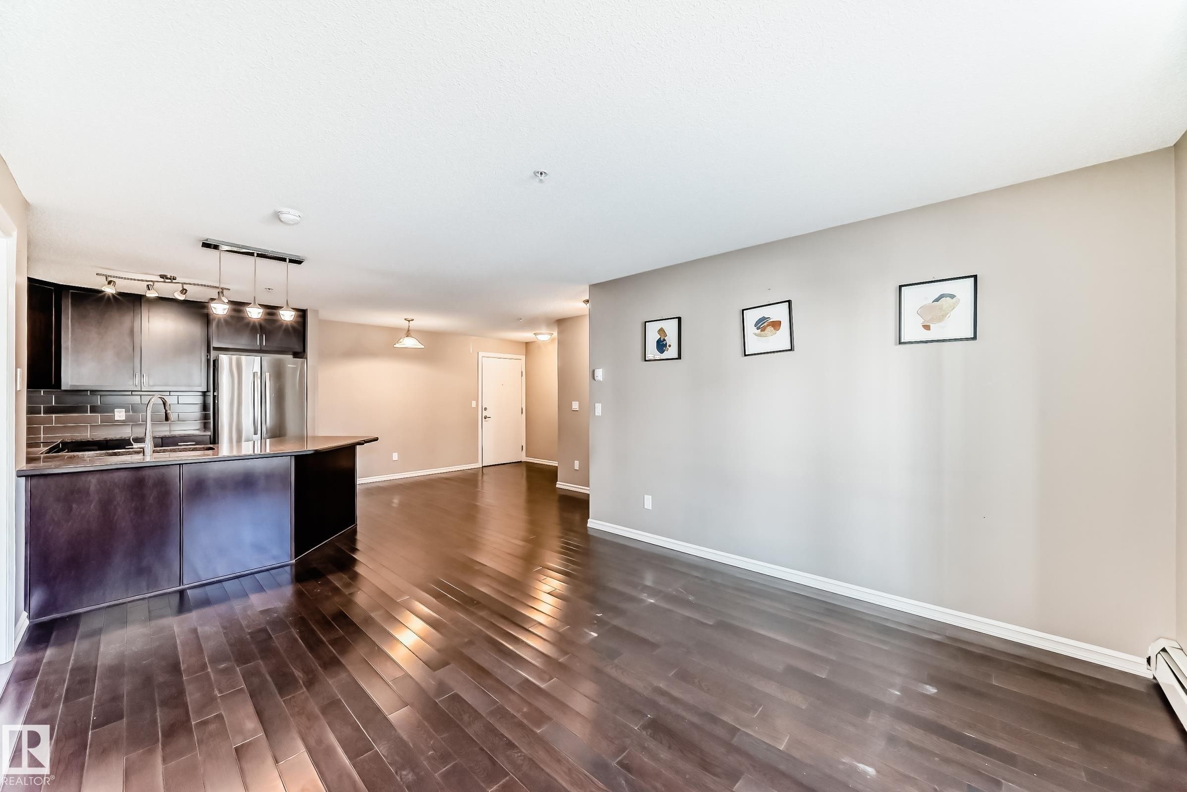 Open concept living area featuring dark wood flooring, light-colored walls, and a kitchen with dark cabinetry, a dark backsplash, and stainless steel appliances - 208 2204 44 Ave, Edmonton, AB - Indoor Photo Showing Kitchen