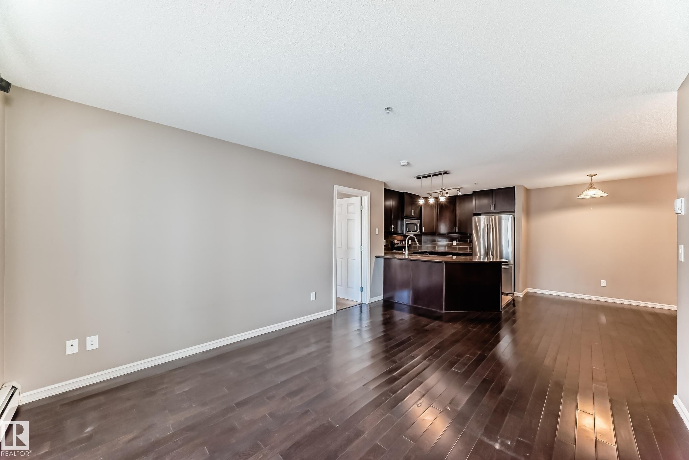 The property features dark hardwood flooring throughout, a kitchen with dark cabinetry and stainless steel appliances, and a kitchen island with a sink - 208 2204 44 Ave, Edmonton, AB - Indoor