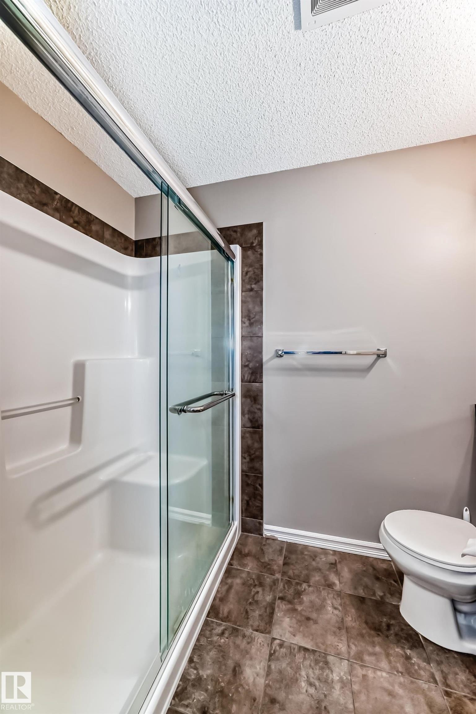 This bathroom features a shower with sliding glass doors, a white toilet, and dark tiled flooring - 208 2204 44 Ave, Edmonton, AB - Indoor Photo Showing Bathroom