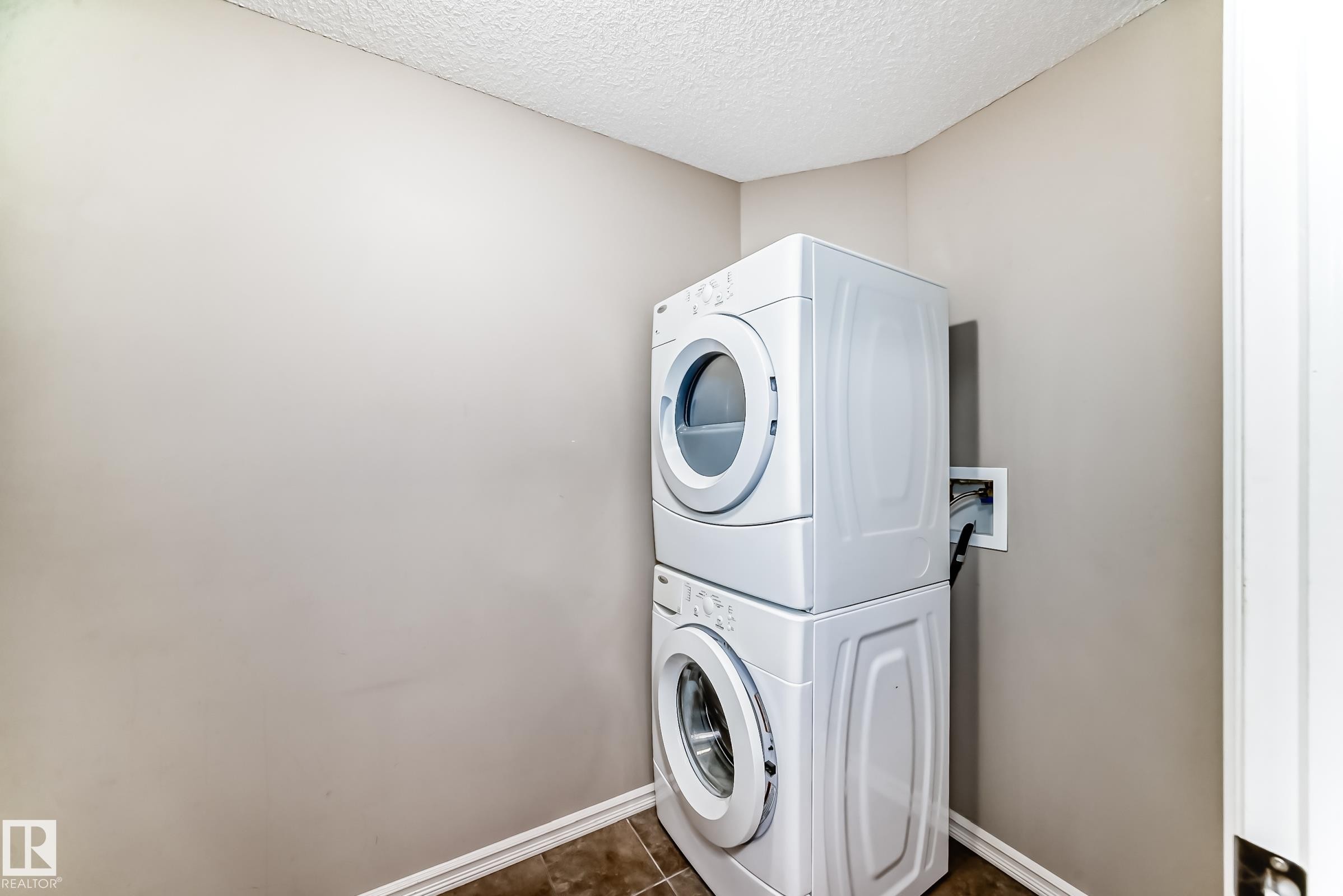 This utility area features a stacked washer and dryer, tile flooring, and light-colored walls - 208 2204 44 Ave, Edmonton, AB - Indoor Photo Showing Laundry Room