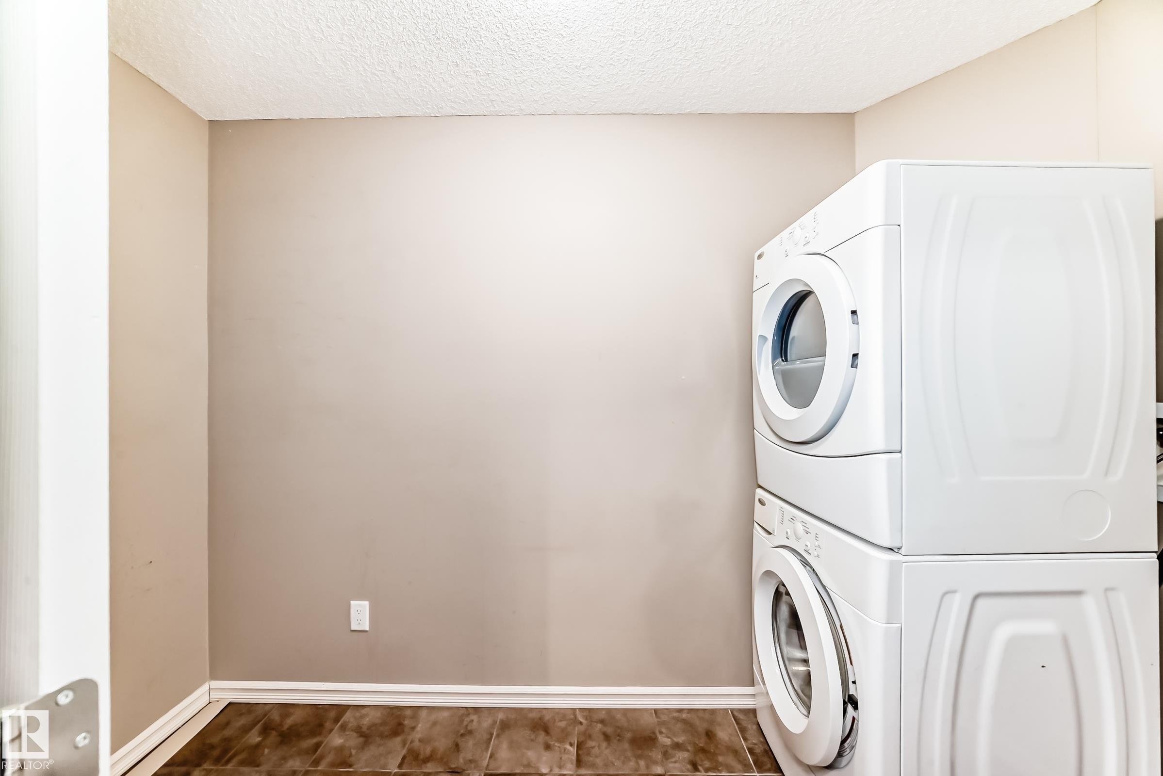 Dedicated laundry area featuring a stacked washer and dryer, tile flooring, and neutral-toned walls - 208 2204 44 Ave, Edmonton, AB - Indoor Photo Showing Laundry Room