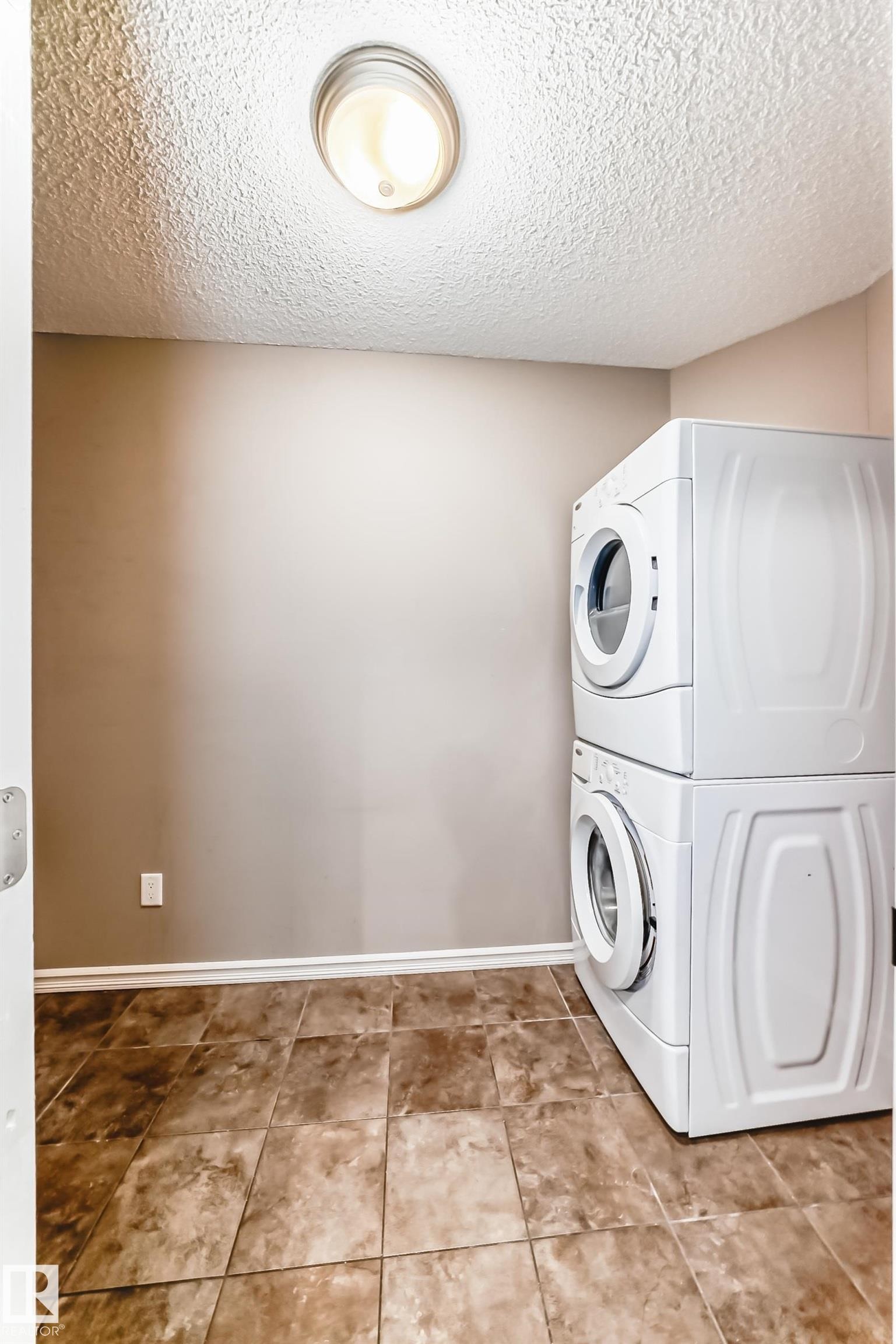 Laundry area featuring tile flooring, neutral wall tones, and a stacked washer and dryer unit - 208 2204 44 Ave, Edmonton, AB - Indoor Photo Showing Laundry Room